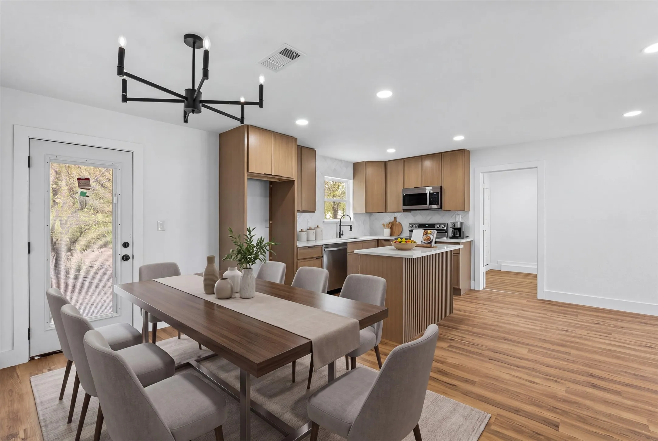 Open-concept living area featuring wood-finish flooring, a modern chandelier, light wood cabinetry, white countertops, and a full-light exterior door