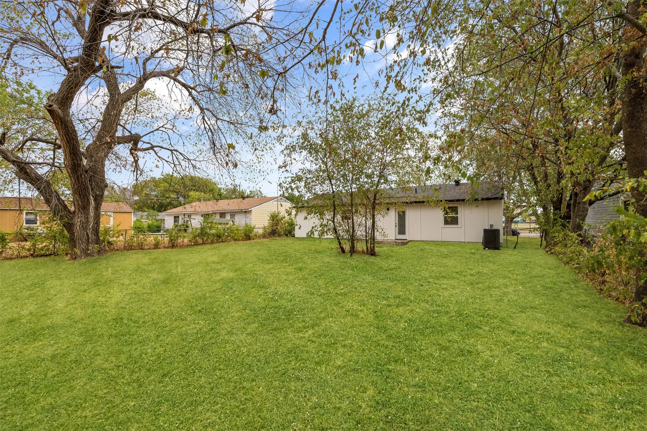 Expansive green lawn with mature trees and a single-story residence featuring a dark roof