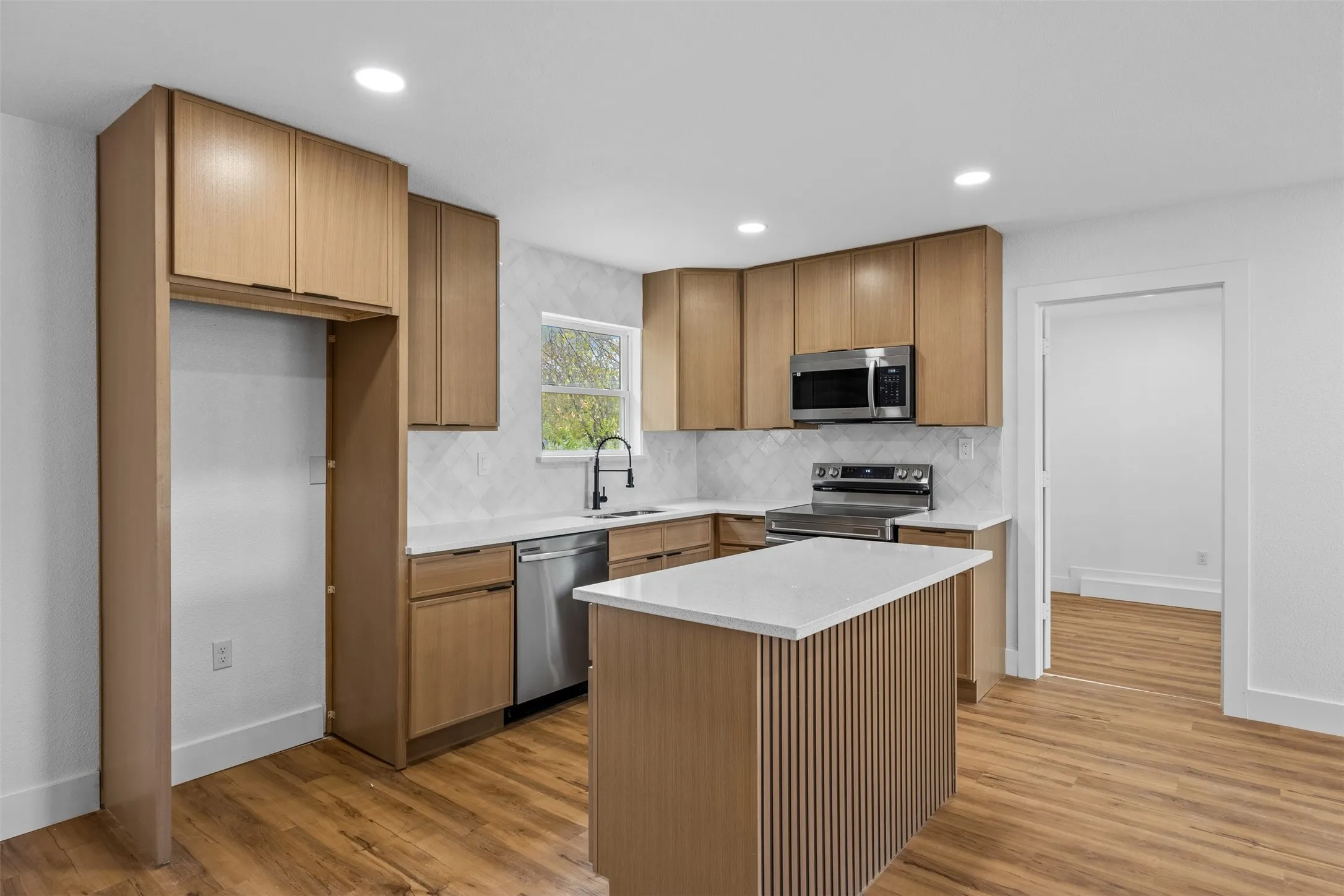 Modern kitchen featuring wood-finish cabinetry, stainless steel appliances, a white quartz countertop island, and wood-finish flooring
