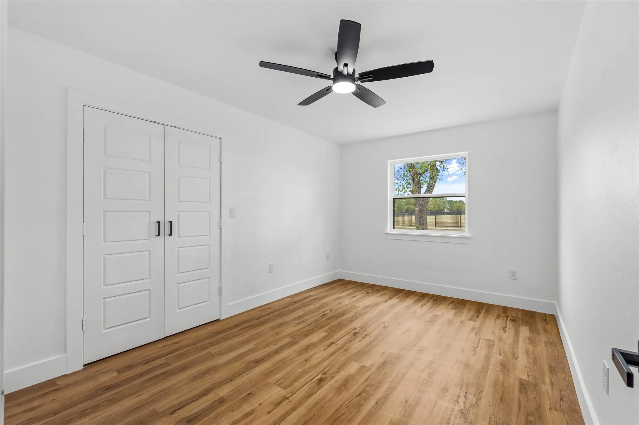 Wood-finish flooring, white paneled double doors, black ceiling fan with integrated lighting, and a white-framed window