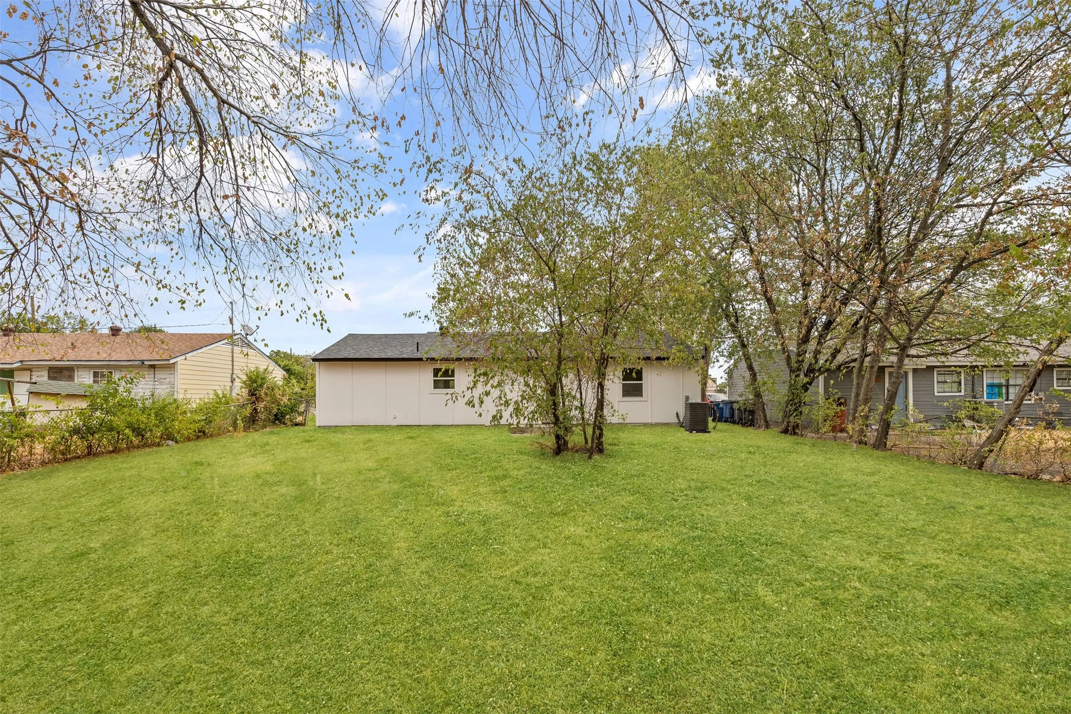 Expansive rear lawn featuring a white-sided exterior, dark shingle roof, and mature trees