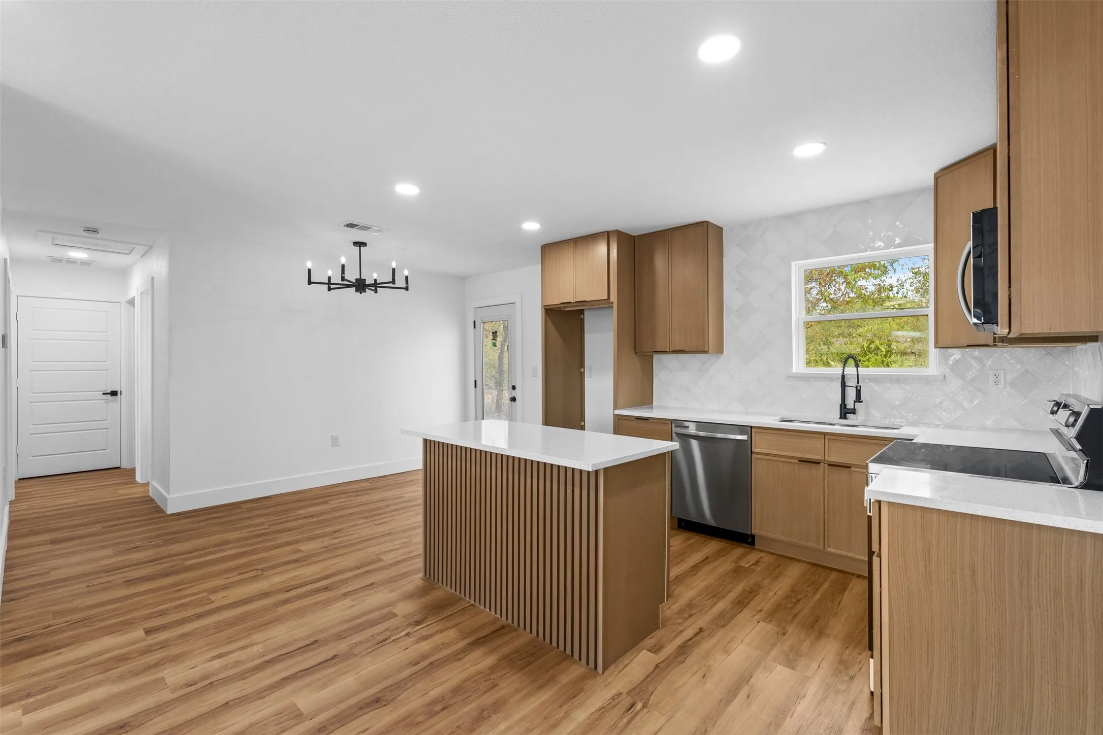 Open-concept kitchen and dining area featuring wood-finish flooring, a kitchen island with slatted paneling, light wood cabinetry, white countertops, and stainless steel appliances