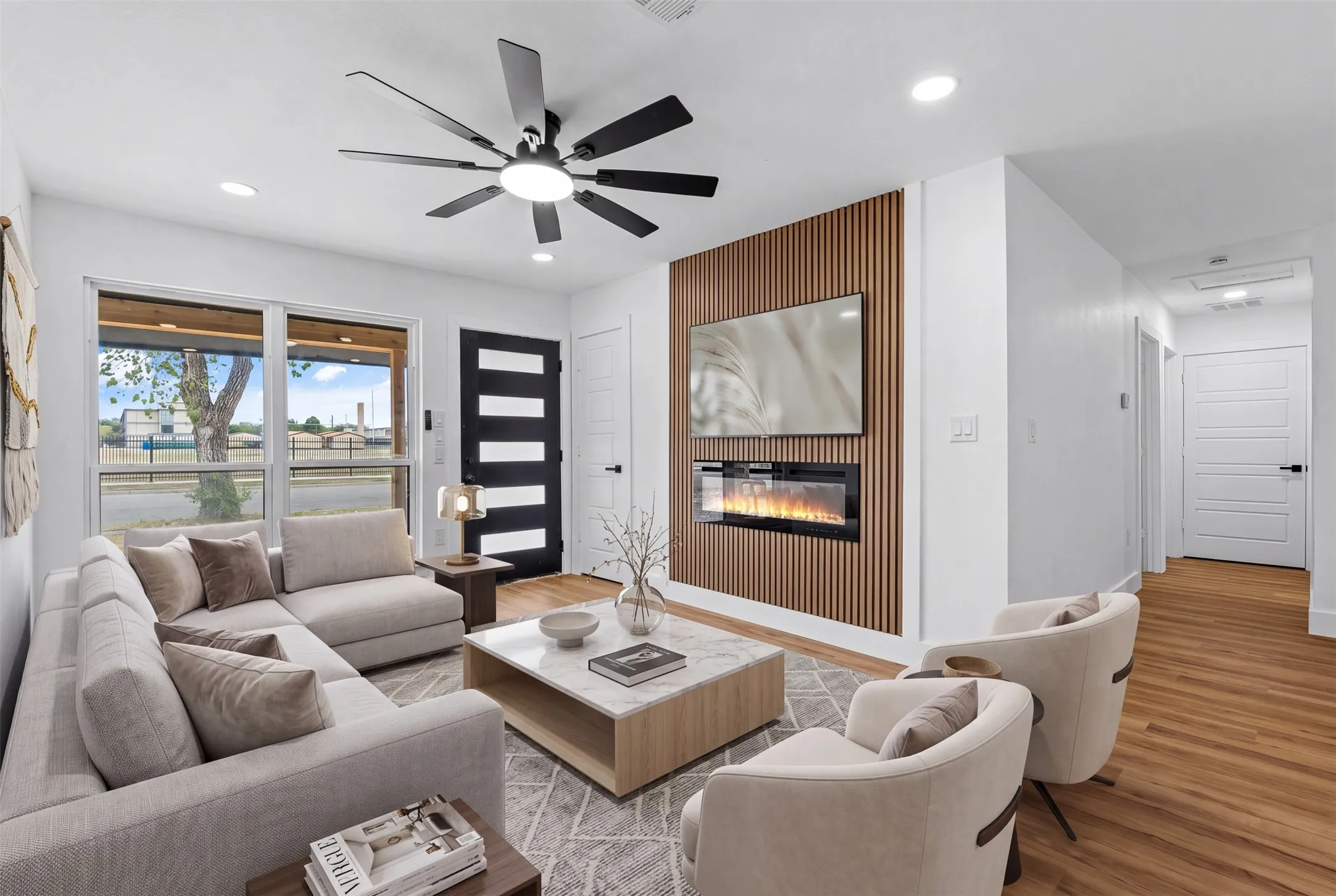 Recessed lighting, wood-finish flooring, a modern ceiling fan, an accent wall with an electric fireplace, and large windows