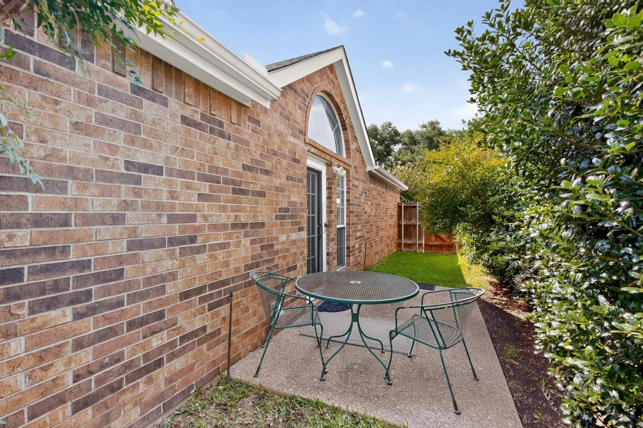 Brick exterior with white gutters, arched window above a glass-paned door, concrete patio, and fenced yard