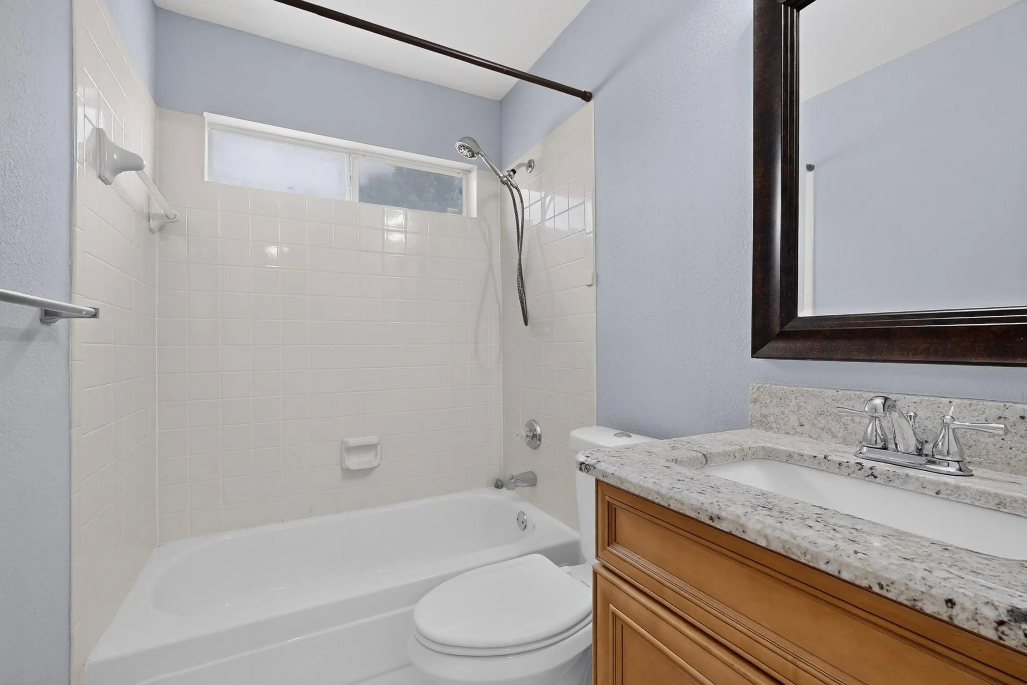 Bathroom featuring a white bathtub, tiled shower surround, frosted window, wood-finish vanity, and speckled countertop