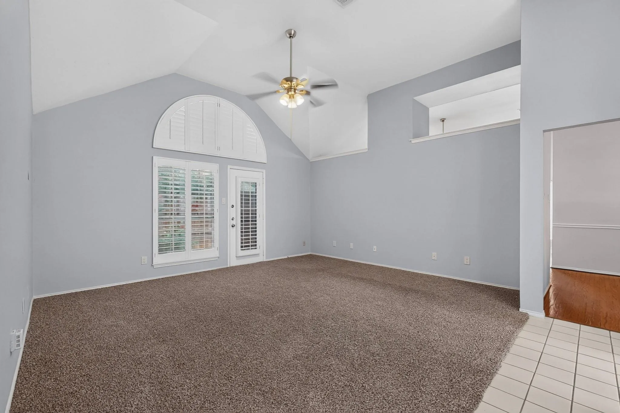 Vaulted ceiling with an illuminated ceiling fan, a window with plantation shutters, a glass-paneled door, and a tiled entry