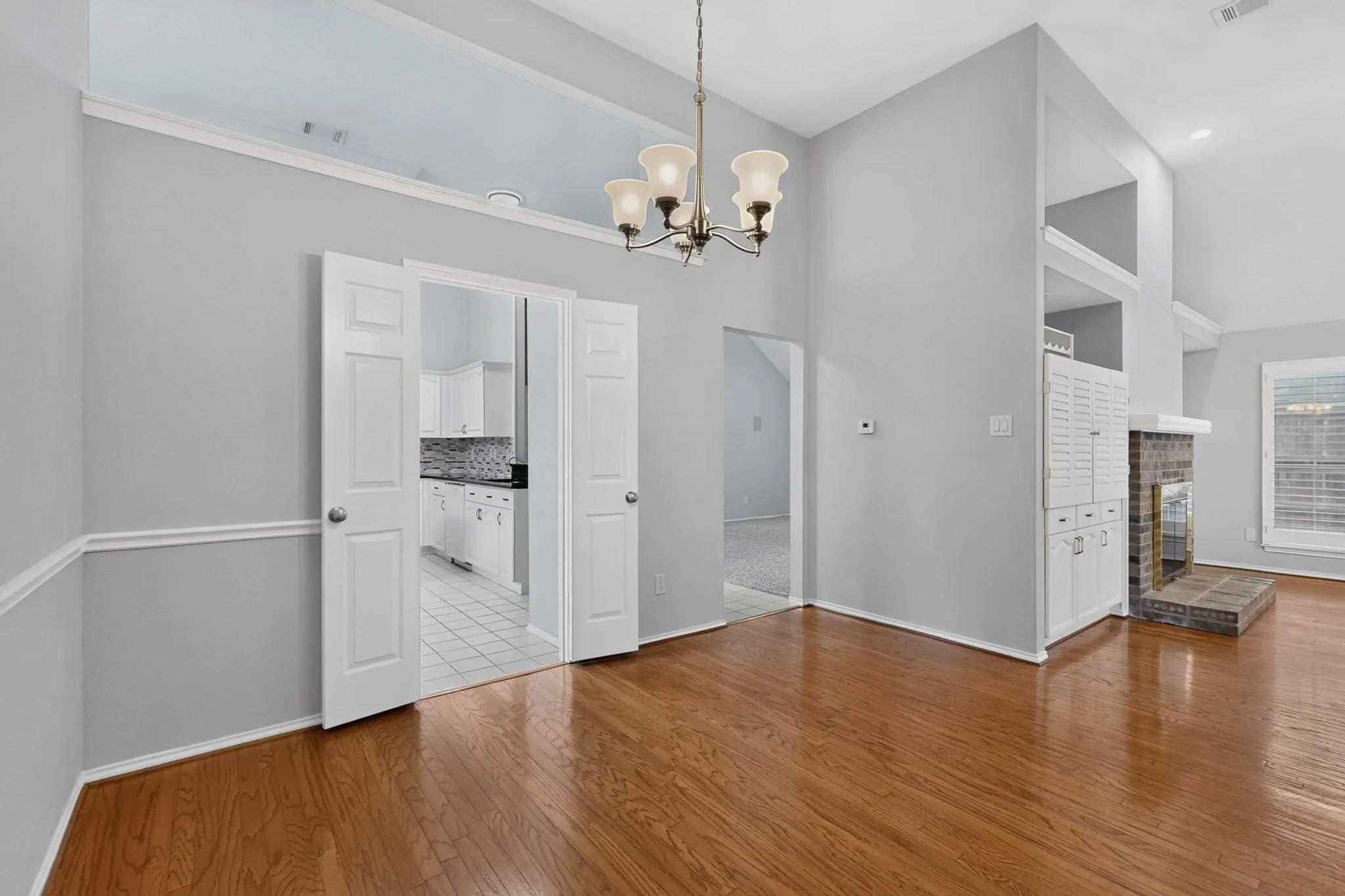 Vaulted ceilings with a chandelier, wood-finish flooring, white double French doors, and a brick fireplace