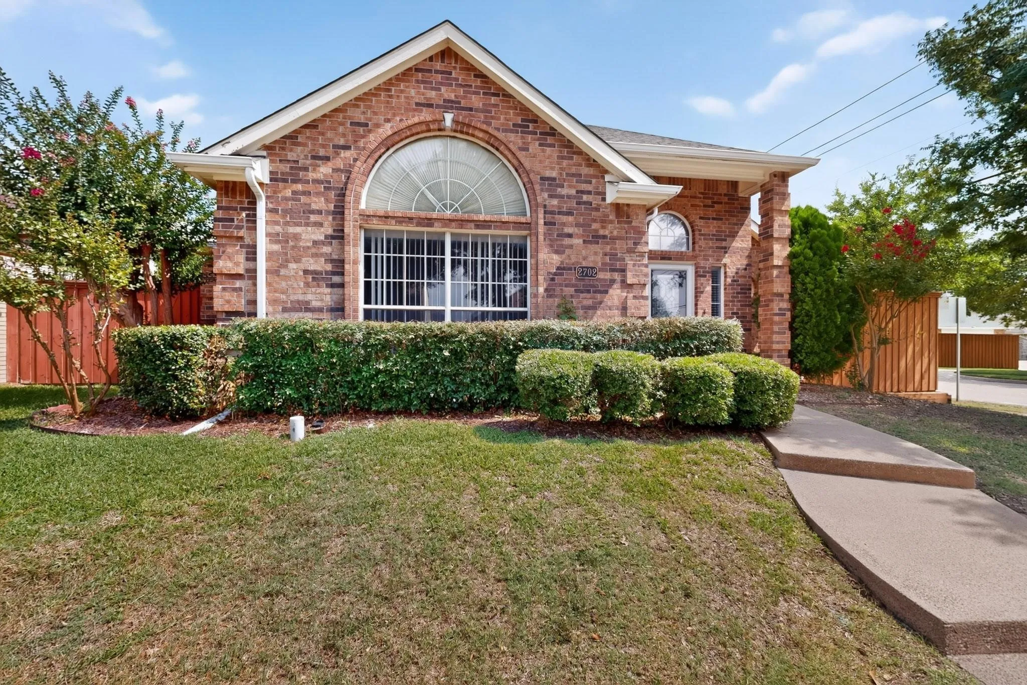 Brick exterior with an arched window, a covered entryway, and mature landscaping