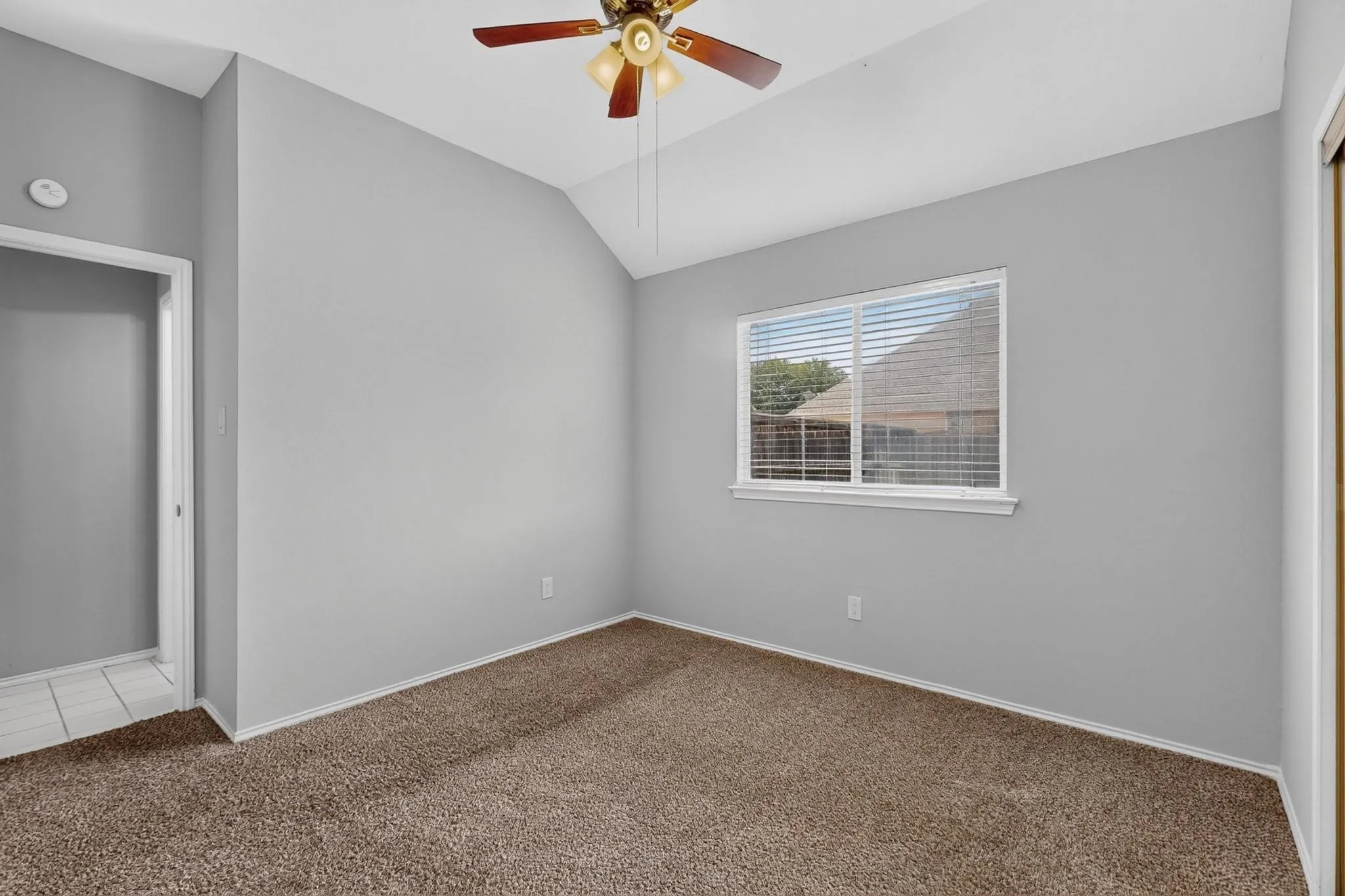 Vaulted ceiling with an attached ceiling fan, single window with blinds, and carpeted flooring