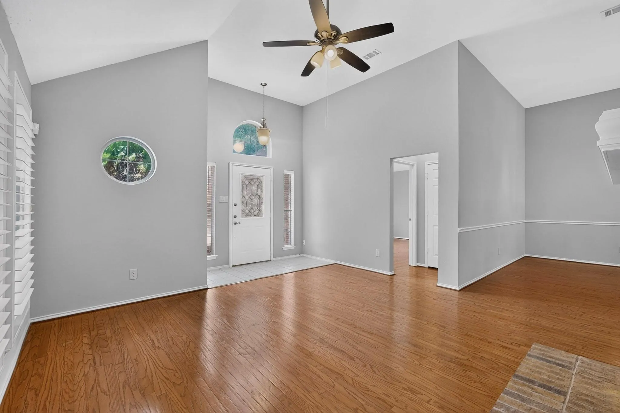 Vaulted ceilings, wood-finish flooring, decorative oval window, arched transom window, and a ceiling fan with integrated lighting