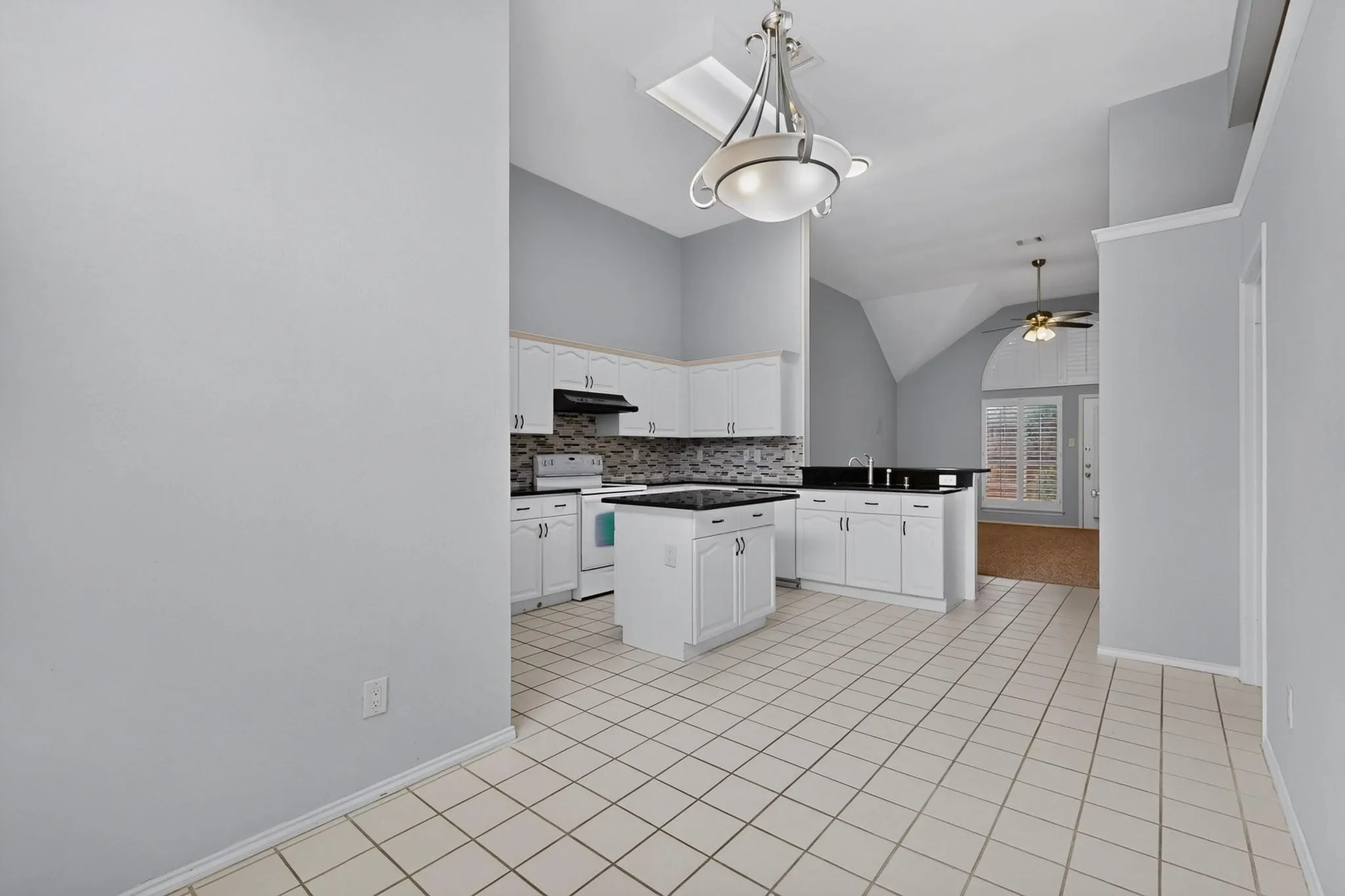 Kitchen featuring white cabinetry, dark countertops, a mosaic tile backsplash, a center island, and tile flooring