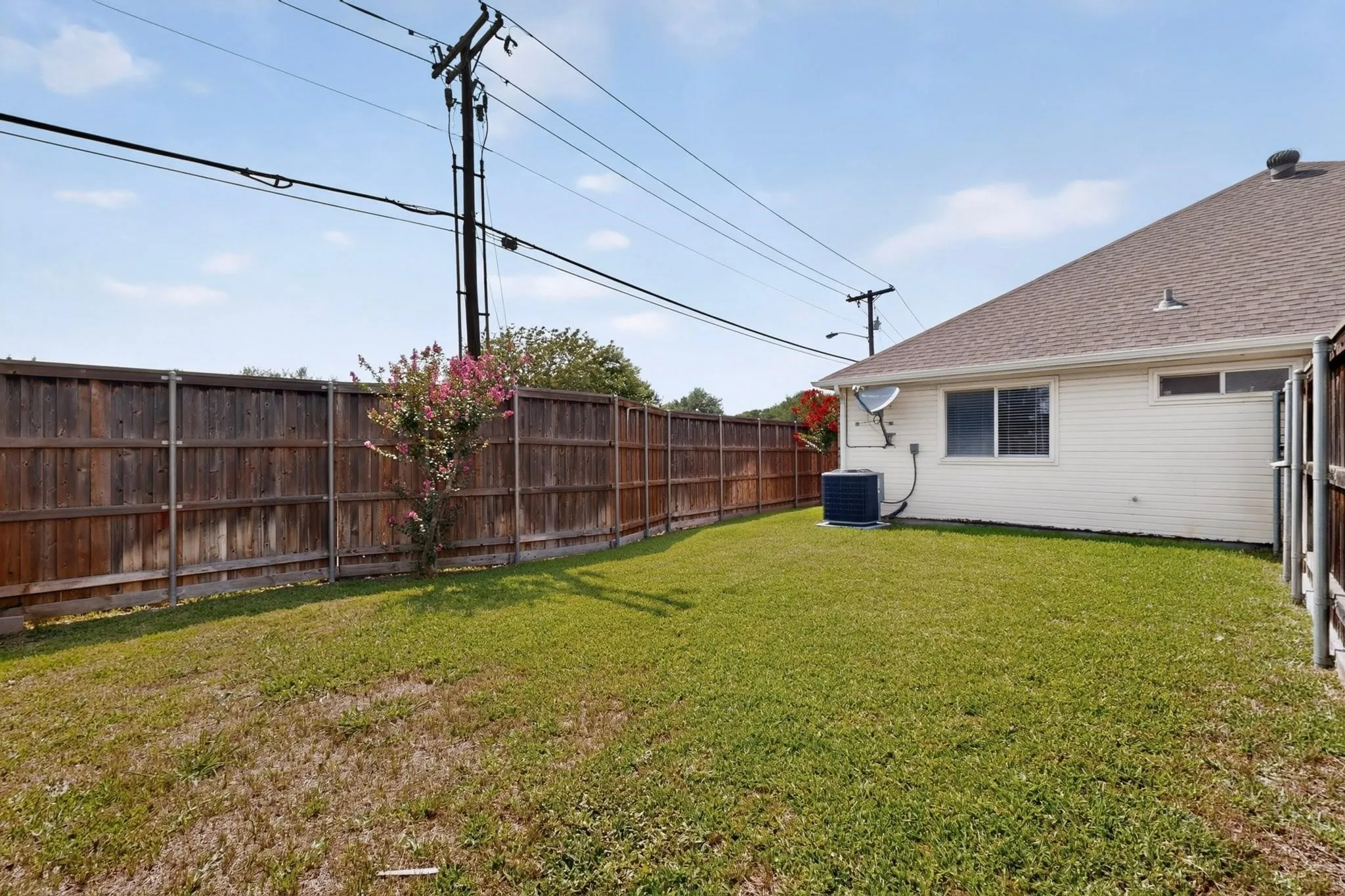 Expansive backyard with a manicured lawn, full wood privacy fence, and a blooming shrub