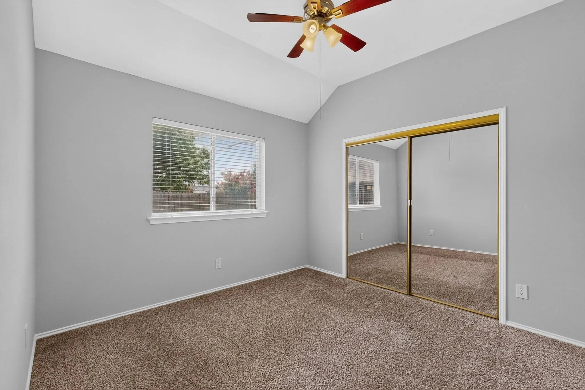 Vaulted ceiling with a ceiling fan, window with blinds, mirrored closet doors, and carpeted flooring