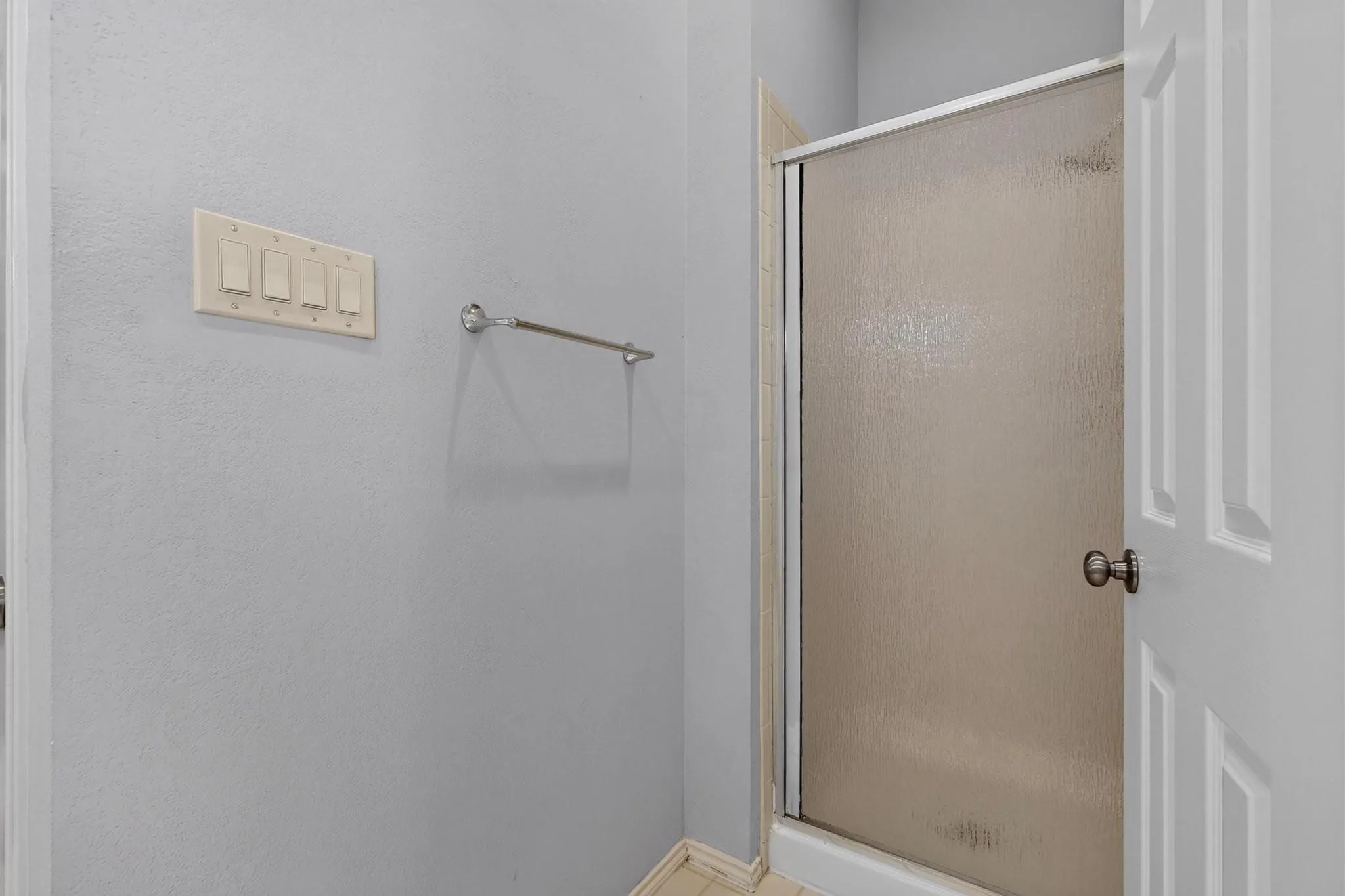 Enclosed shower with frosted glass door, light gray walls, and white trim
