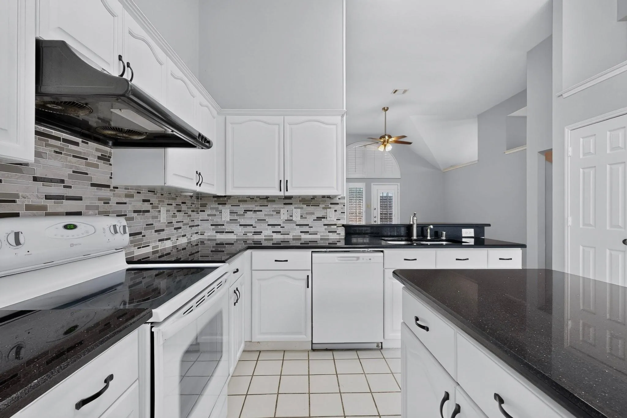 Kitchen featuring white cabinetry, black countertops, tile flooring, a tile backsplash, and white appliances
