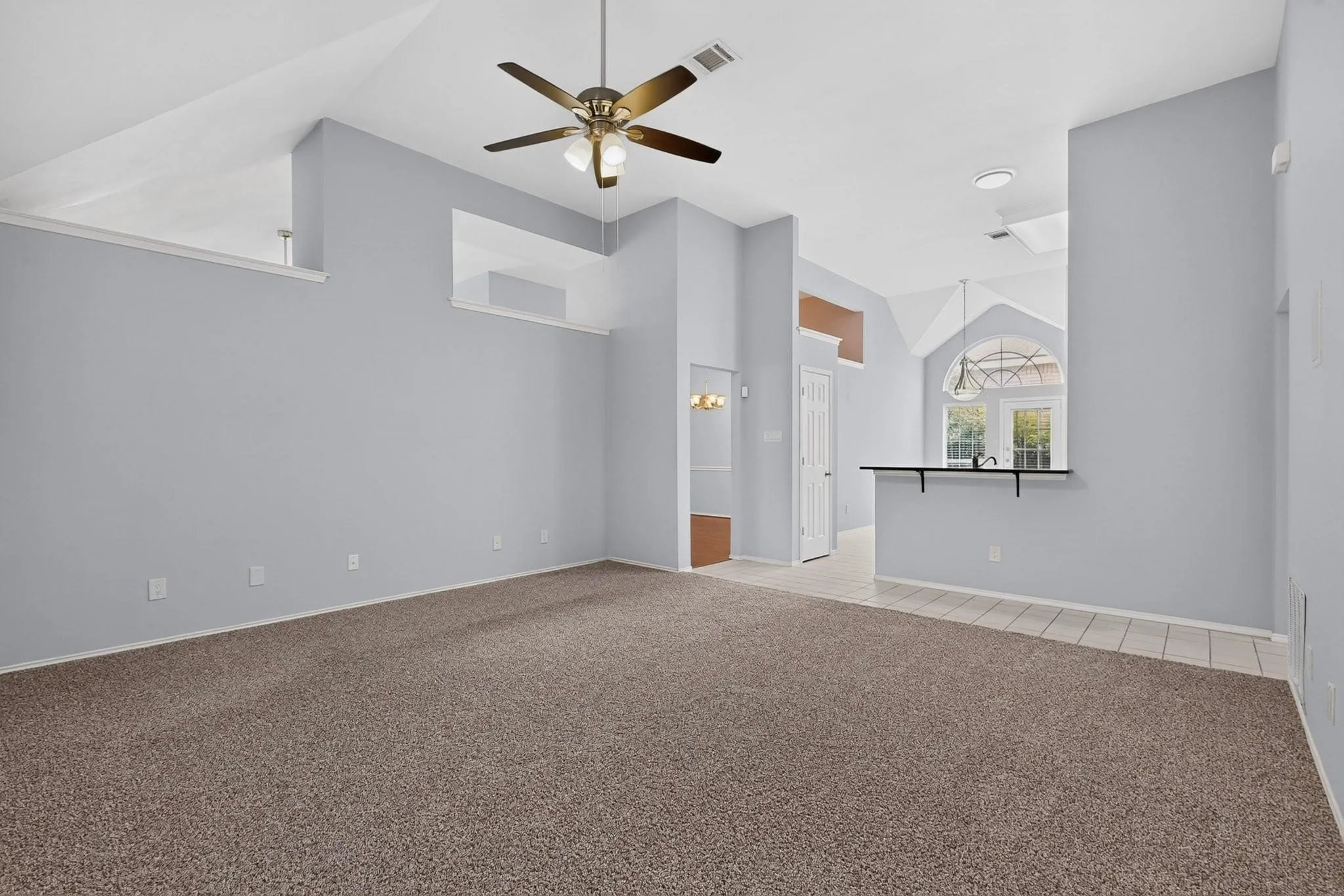 Vaulted ceilings, contemporary ceiling fan, carpet flooring, a breakfast bar with an overhanging countertop, and a tiled entry