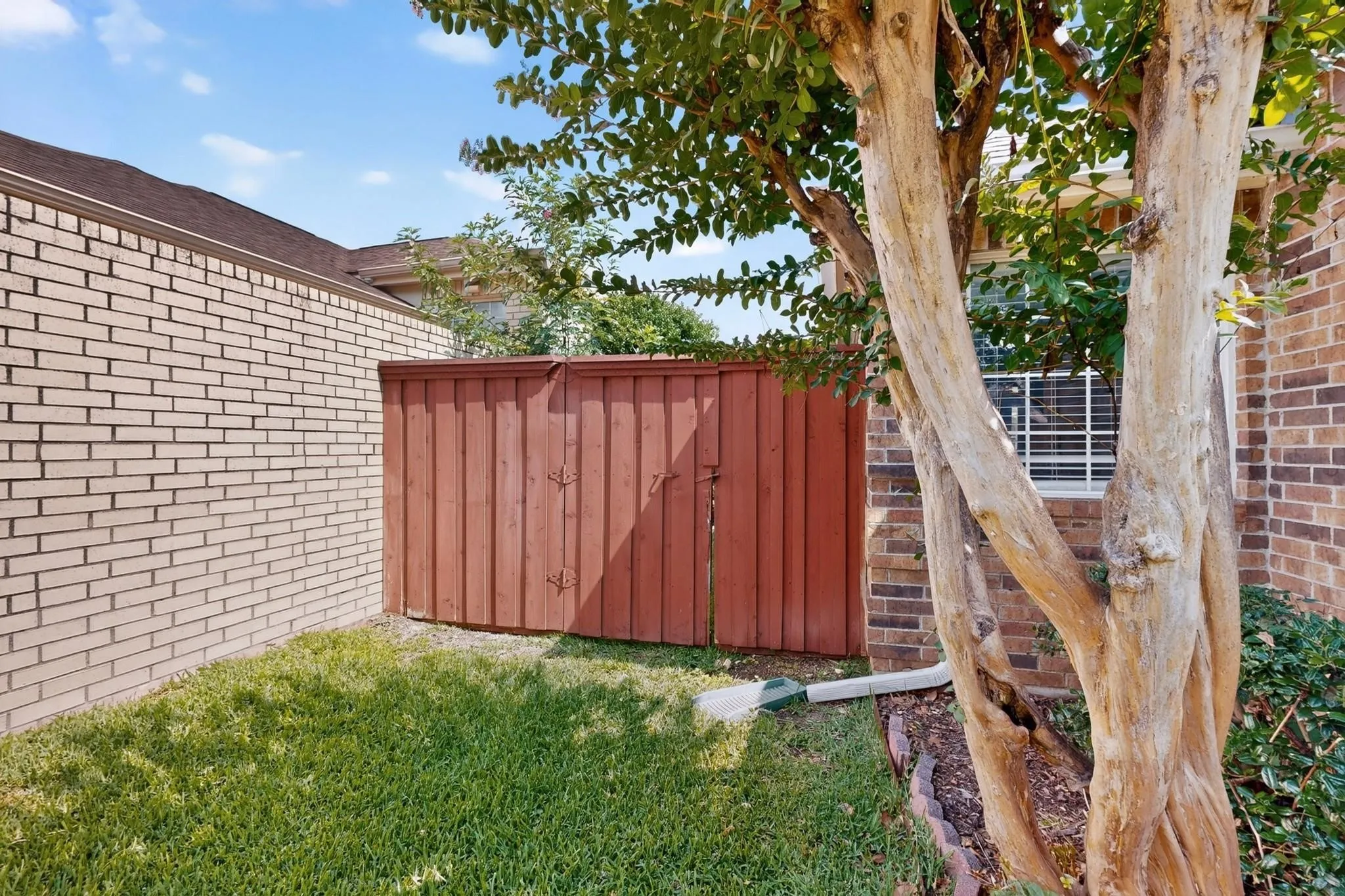 Brick exterior featuring a wood fence, established tree, and green lawn