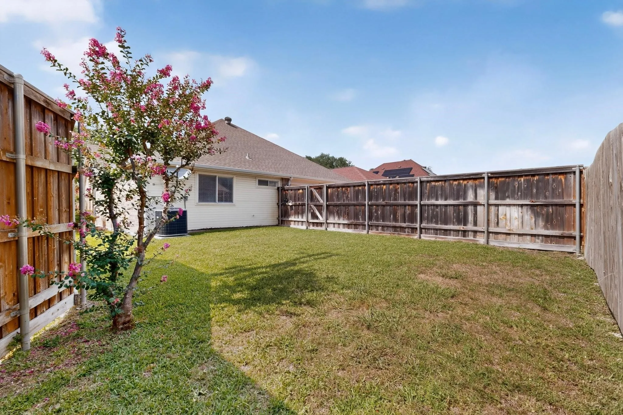 Fenced backyard featuring a manicured lawn, established tree, and a home exterior with a visible window