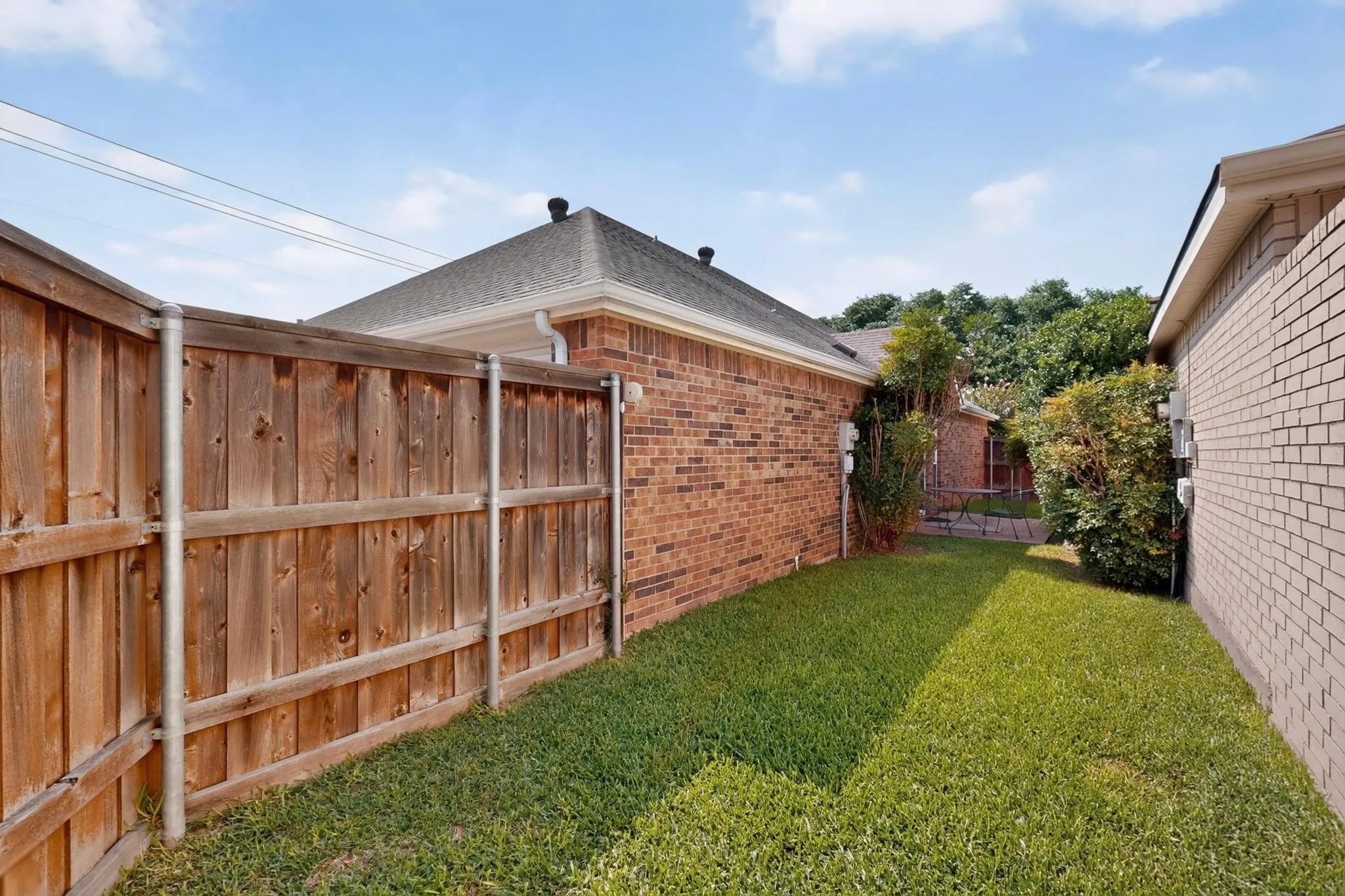 Fenced backyard featuring a wood fence, brick exterior, and a manicured lawn