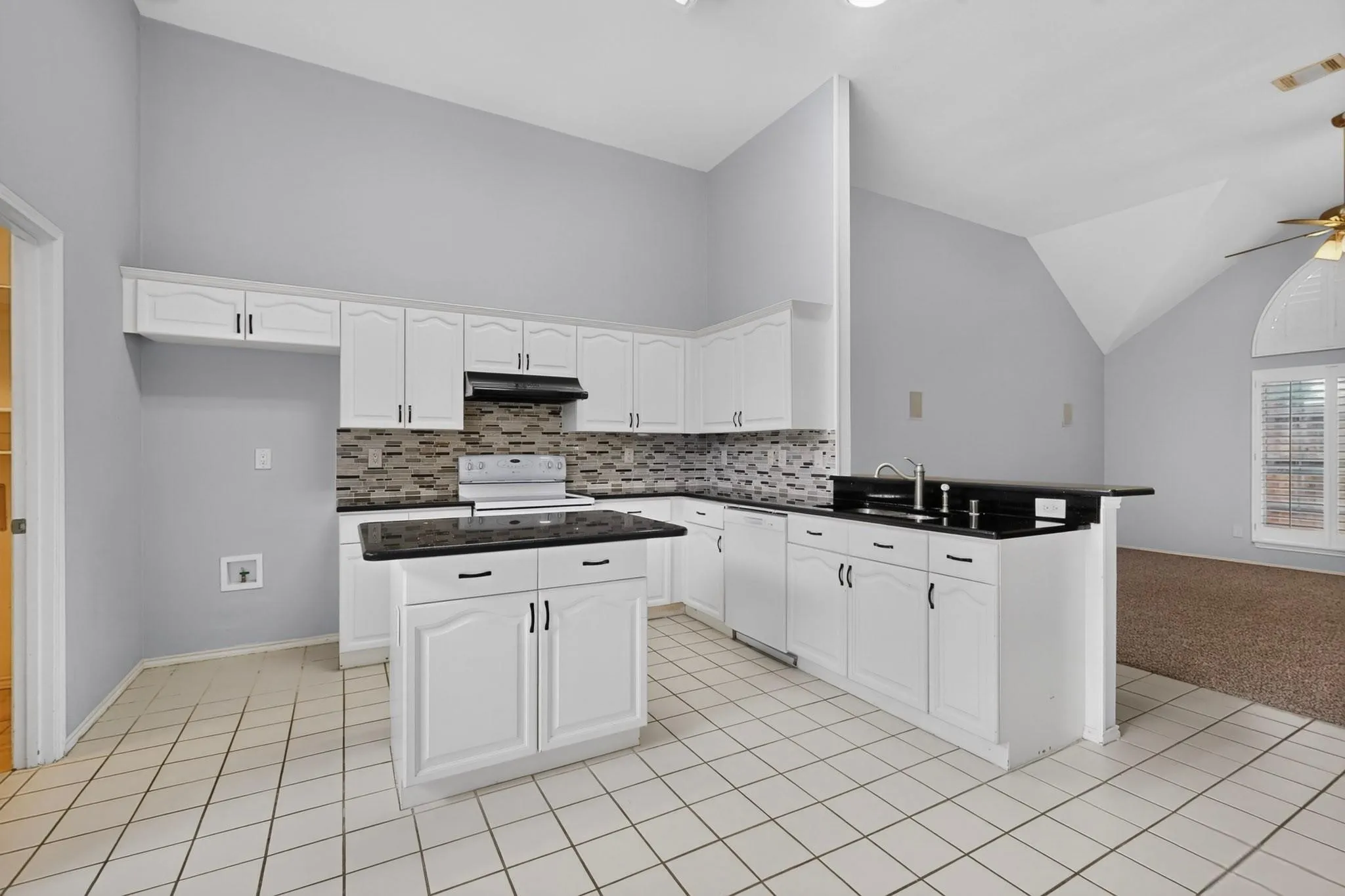 Kitchen featuring white cabinetry, black countertops, a central island, and a tiled backsplash