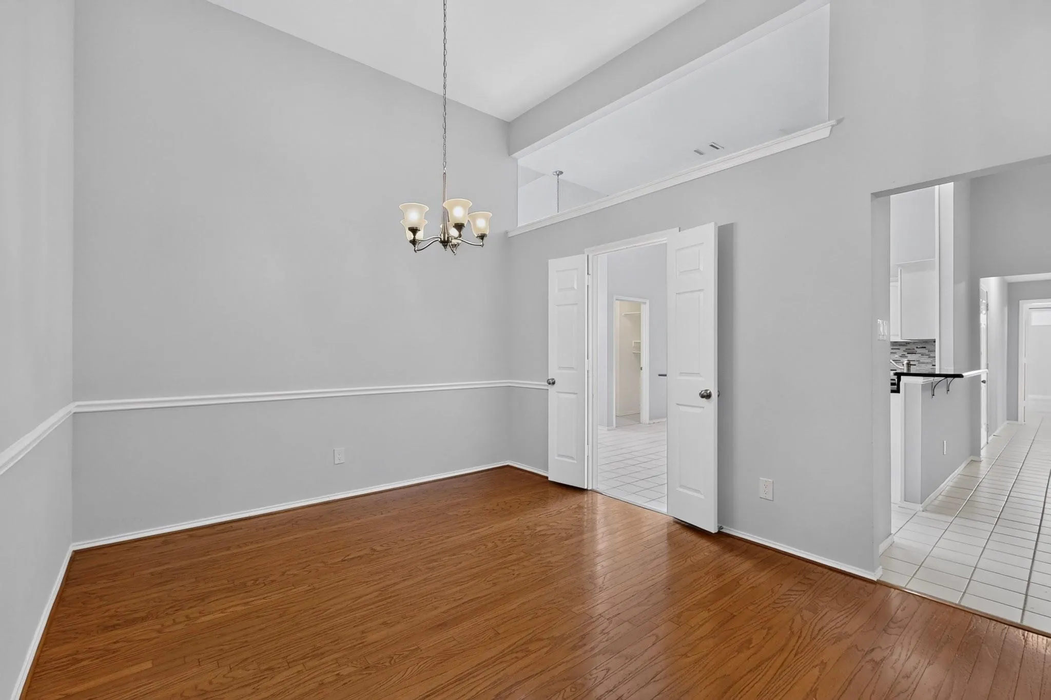 Vaulted ceiling with an attached chandelier, wood-finish flooring, wainscoting, and white bi-fold doors