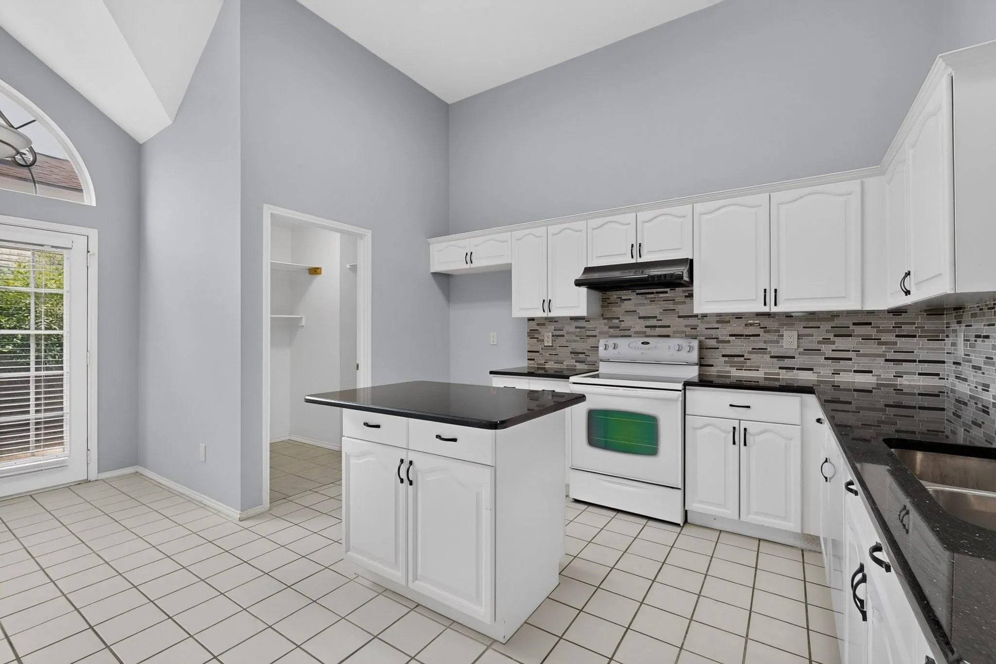 Kitchen featuring vaulted ceilings, white cabinetry, dark countertops, a tiled backsplash, and a central island
