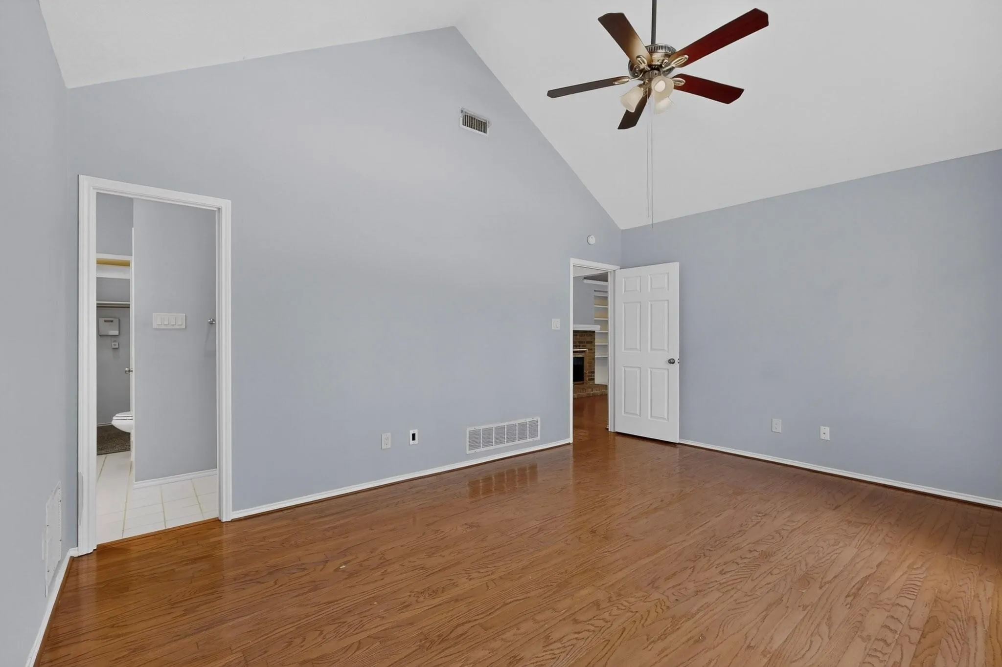 Vaulted ceiling with a ceiling fan, wood-finish flooring, and light-toned wall paint