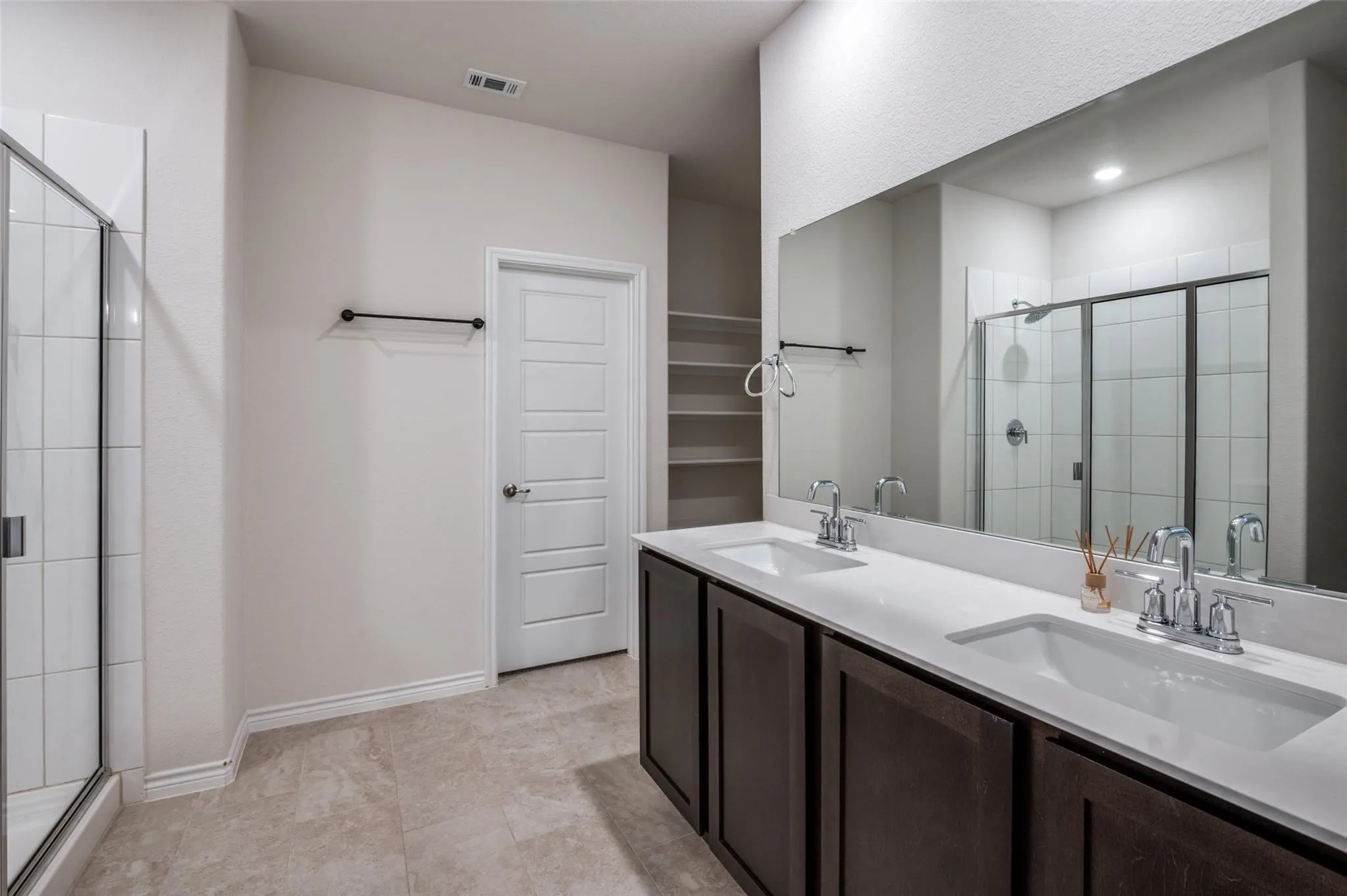 Dual vanity with integrated sinks and chrome fixtures, white countertops, built-in shelving, and a shower with a glass enclosure