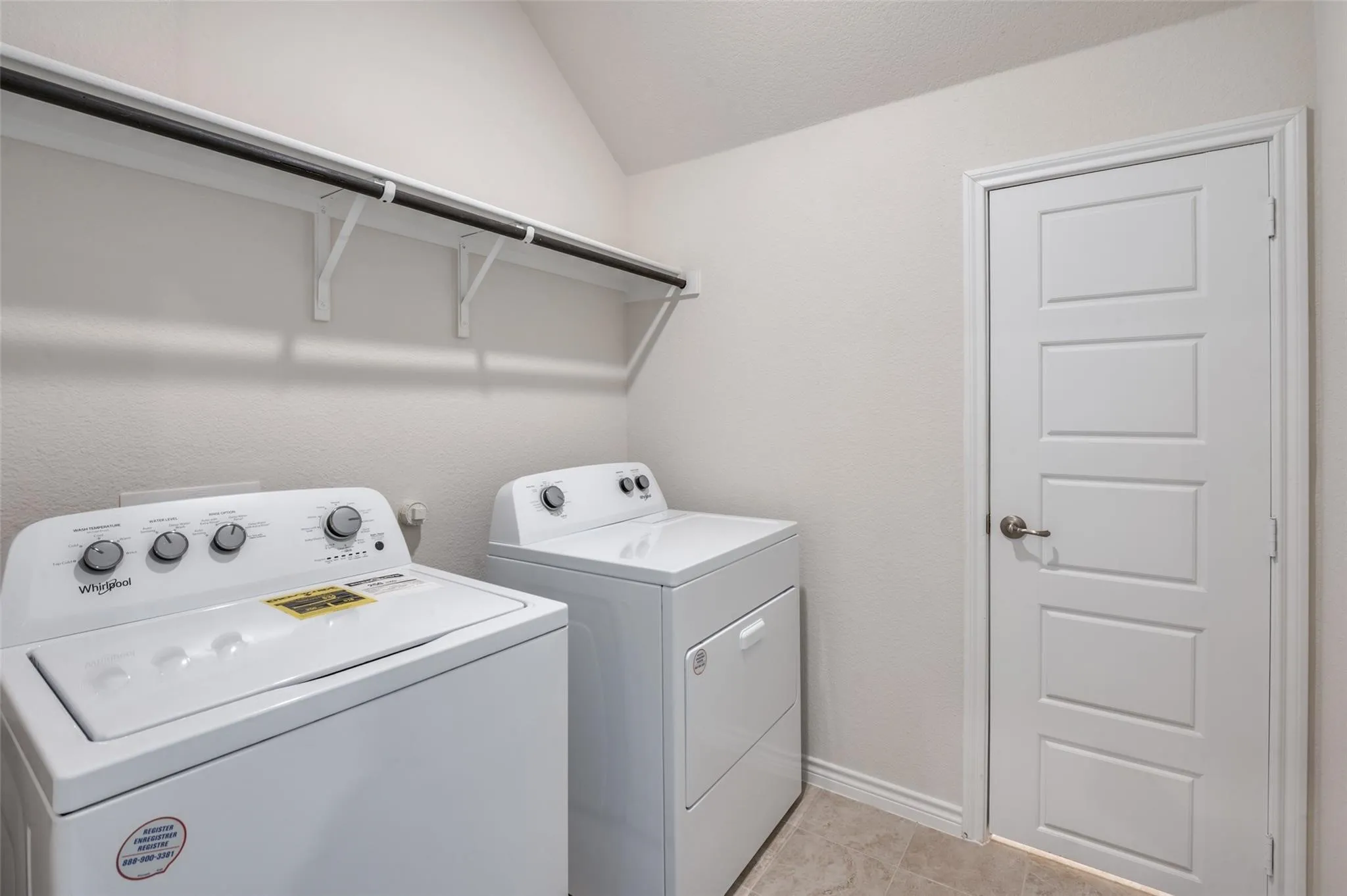 Laundry area with a built-in shelf and hanging rod, tile flooring, and a paneled door