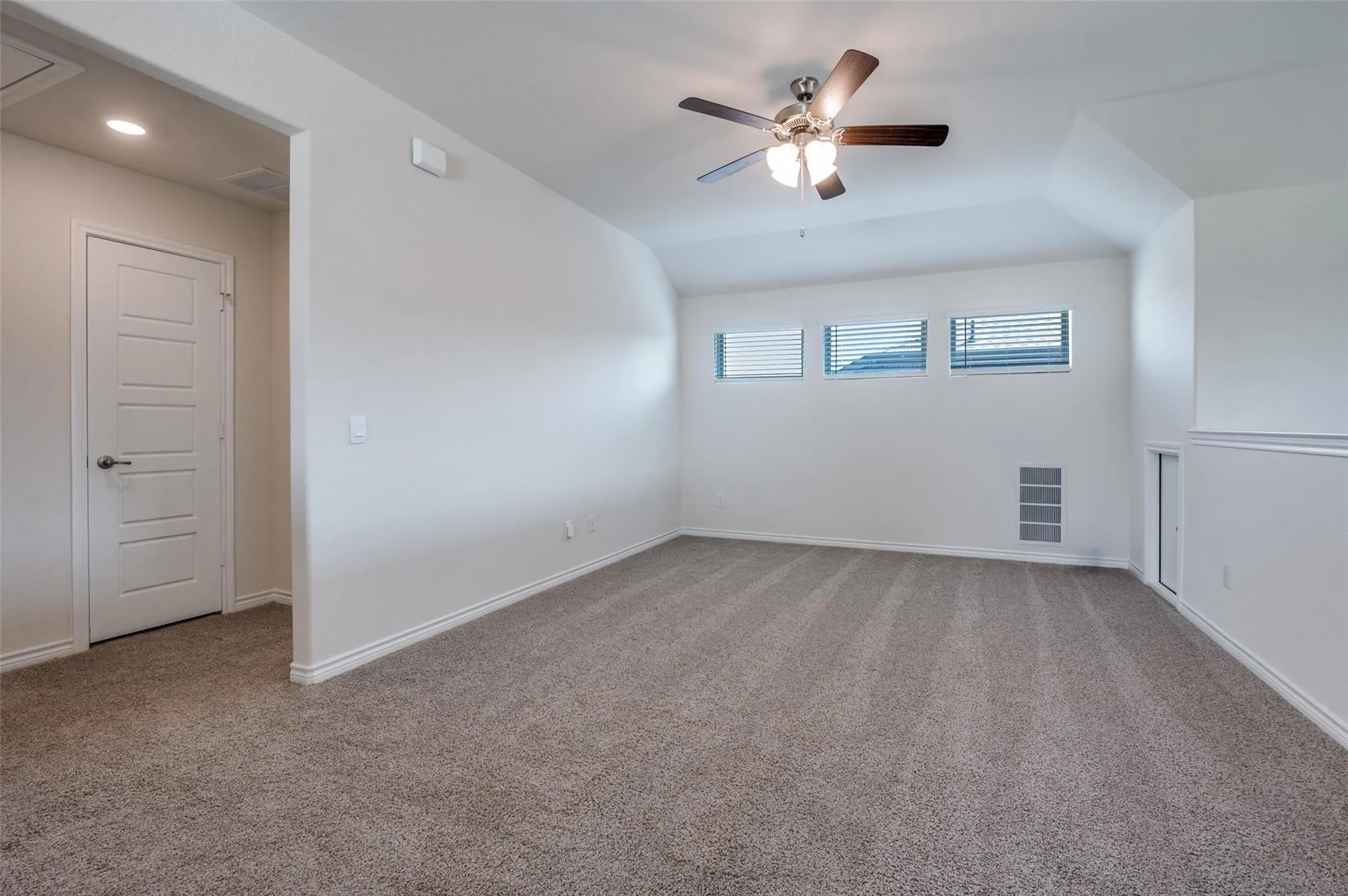Expansive carpeted area featuring a ceiling fan, multiple windows with blinds, and a built-in access panel