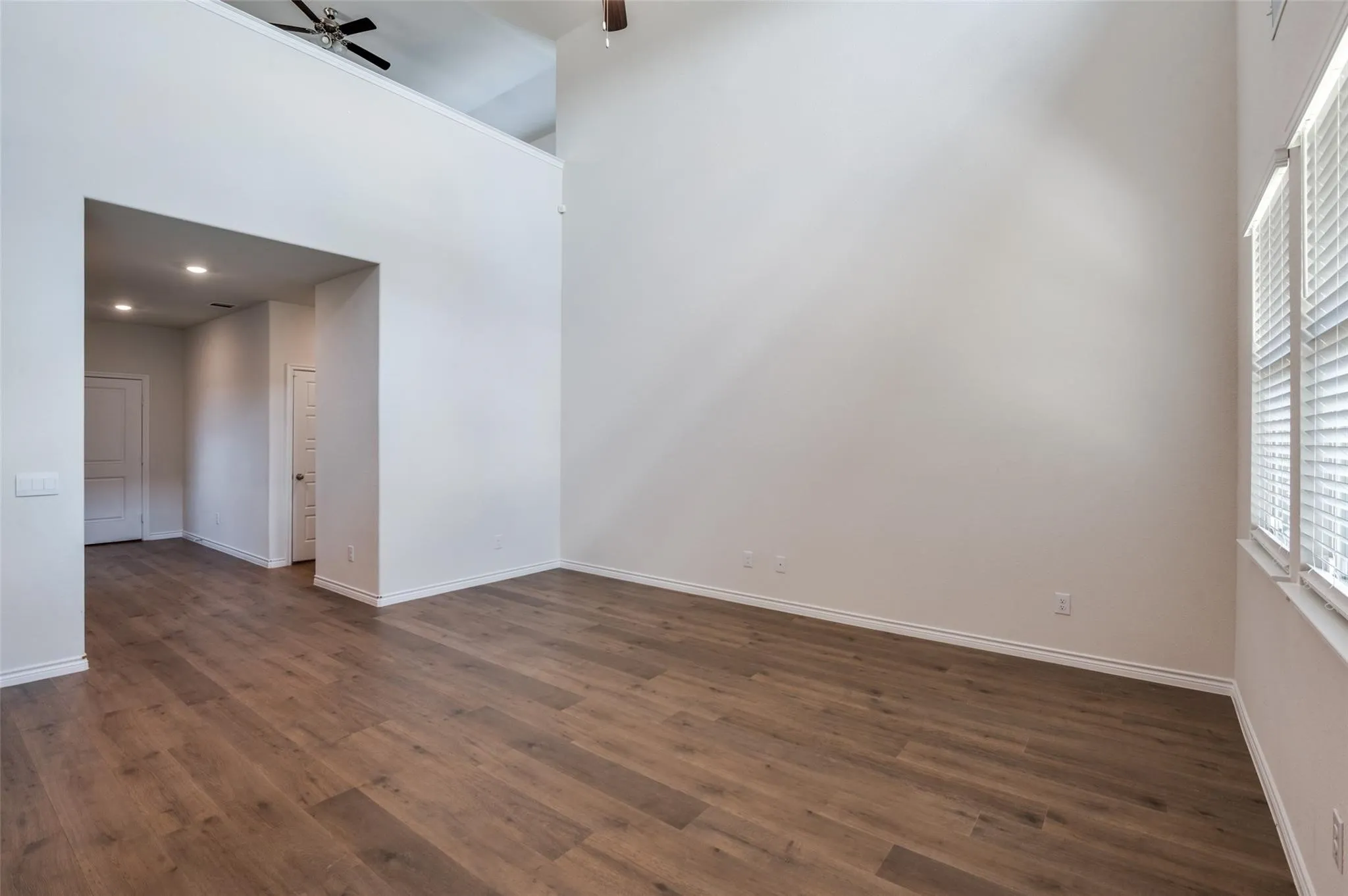 Wood-finish flooring, high ceilings, recessed lighting, window with blinds, and ceiling fan