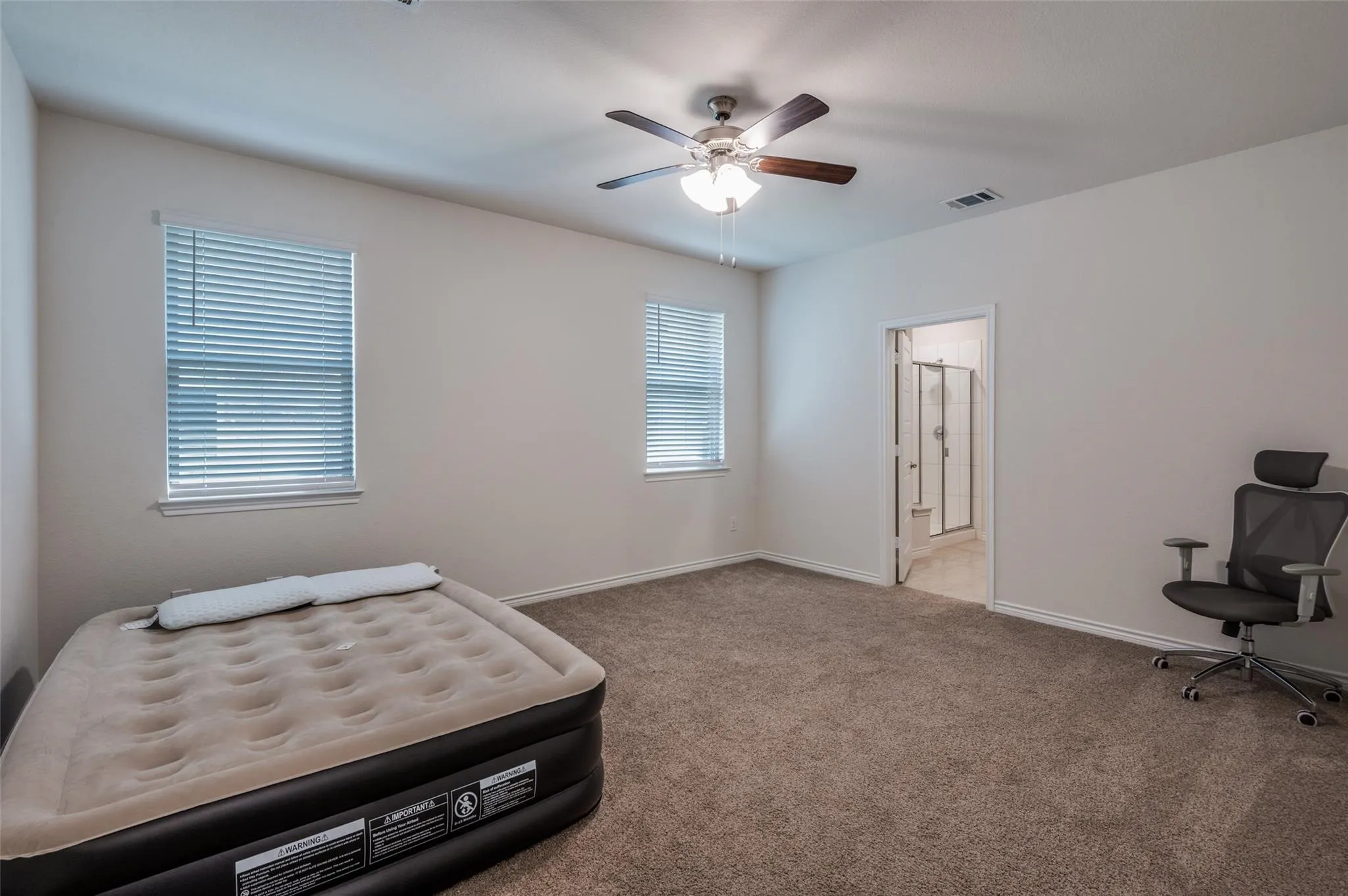 Spacious room with two windows, carpet flooring, and a ceiling fan with integrated lighting