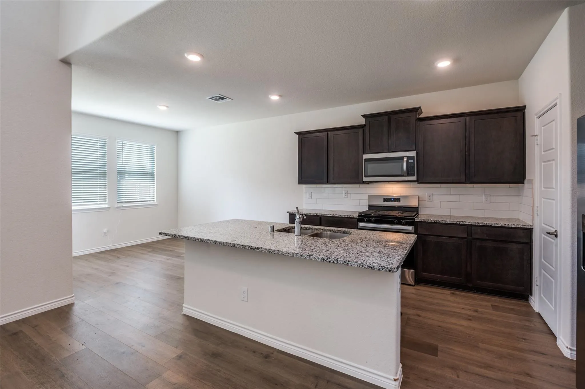 Kitchen with a center island, dark wood-finish cabinetry, stainless steel appliances, granite countertops, and subway tile backsplash