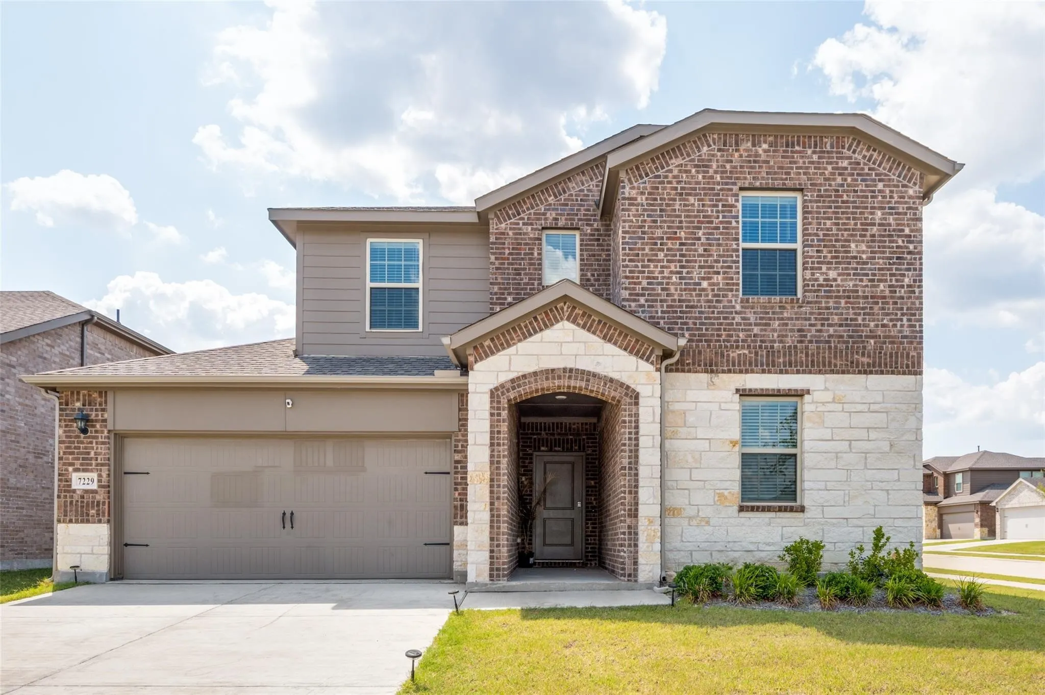 Brick and stone facade, covered entry, attached garage, concrete driveway, and front landscaping