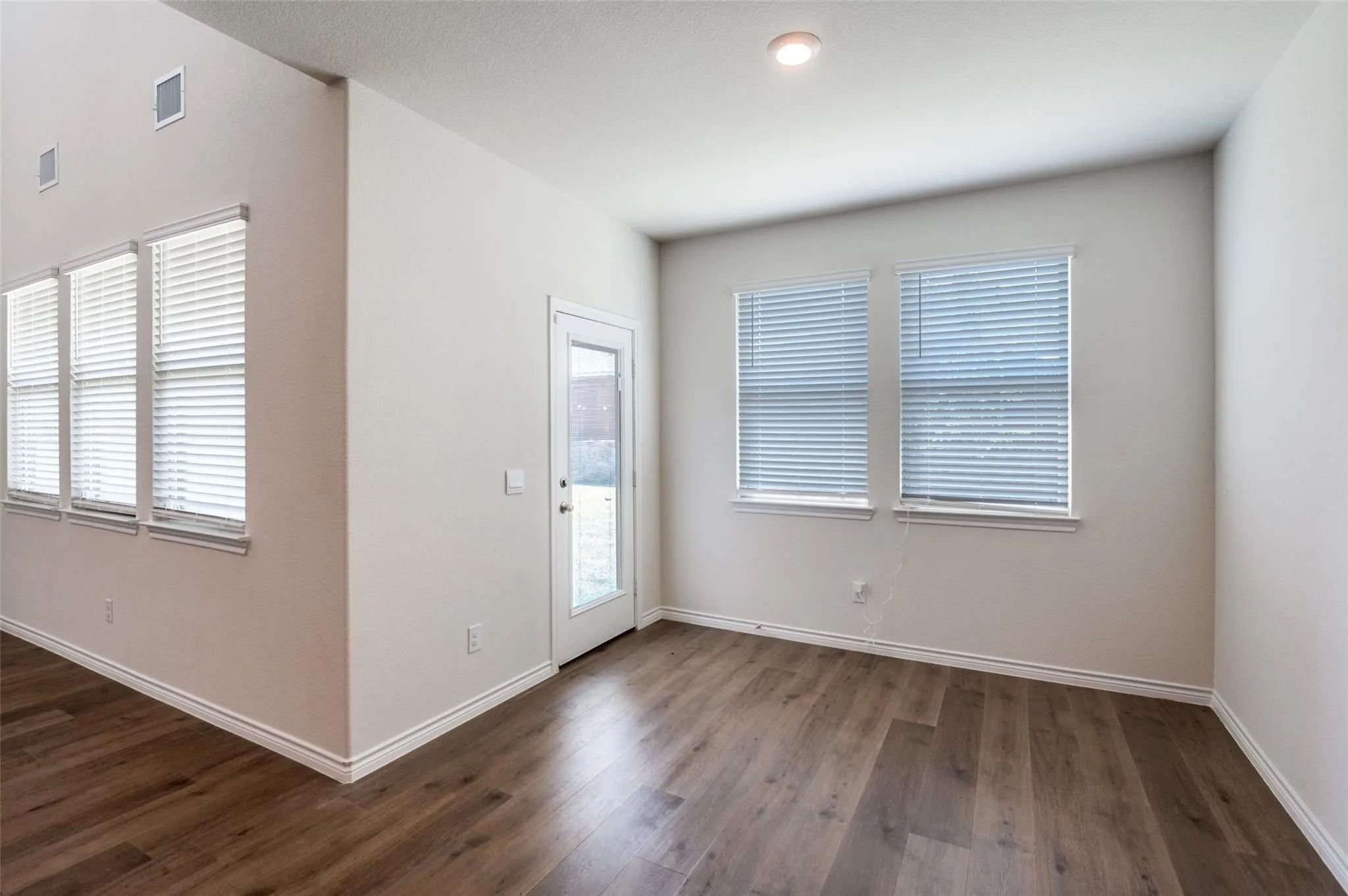Wood-finish flooring, multiple windows with blinds, recessed ceiling lighting, and a glass-paneled exterior door