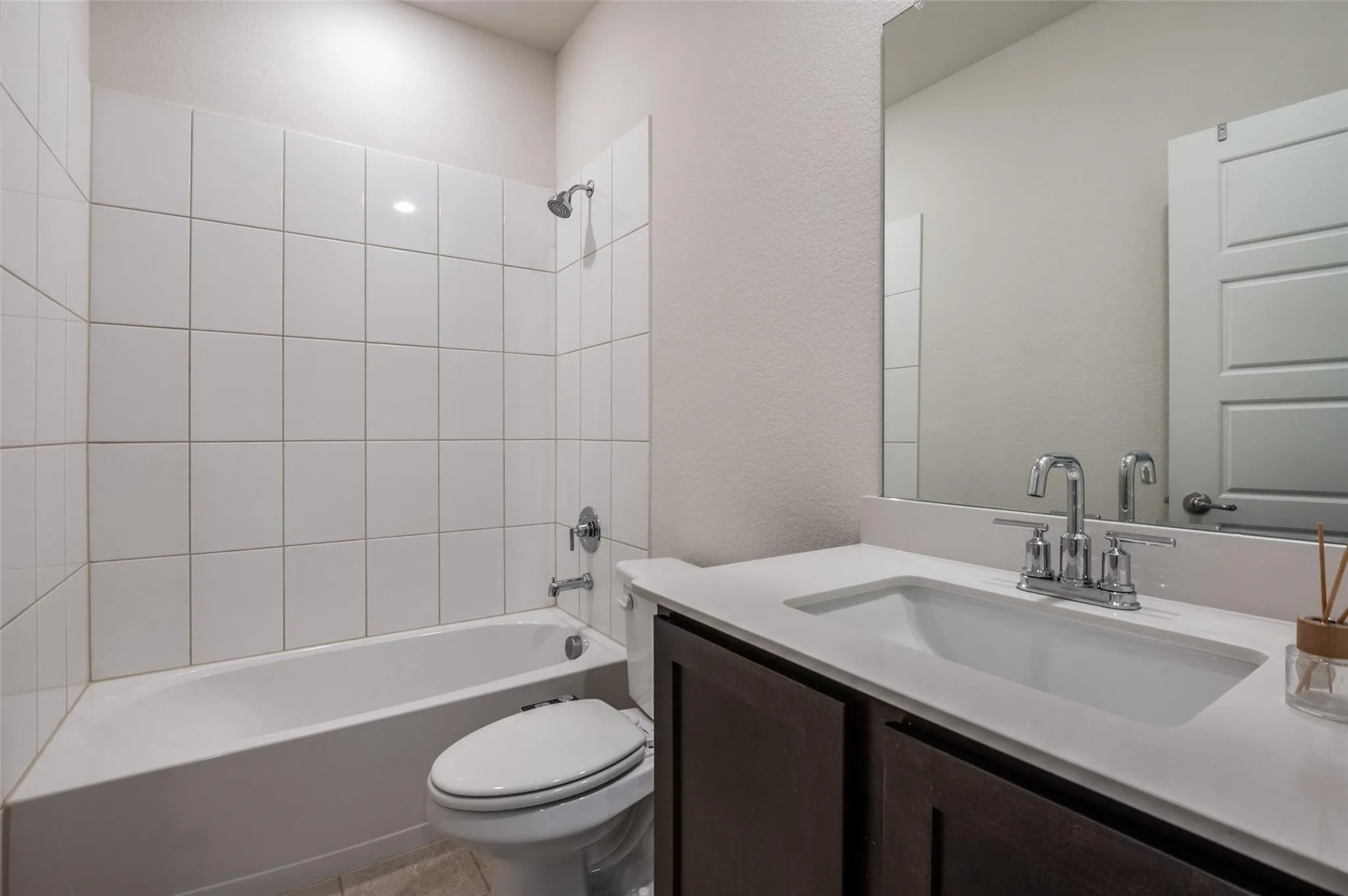 White tile shower surround, integrated bathtub, chrome plumbing fixtures, dark wood-finish vanity, and a rectangular undermount sink with a light-toned countertop