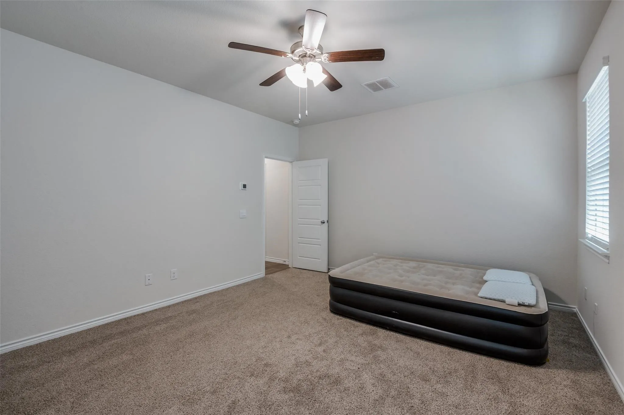 Spacious room featuring neutral carpeting, a ceiling fan with light fixture, and a window with blinds