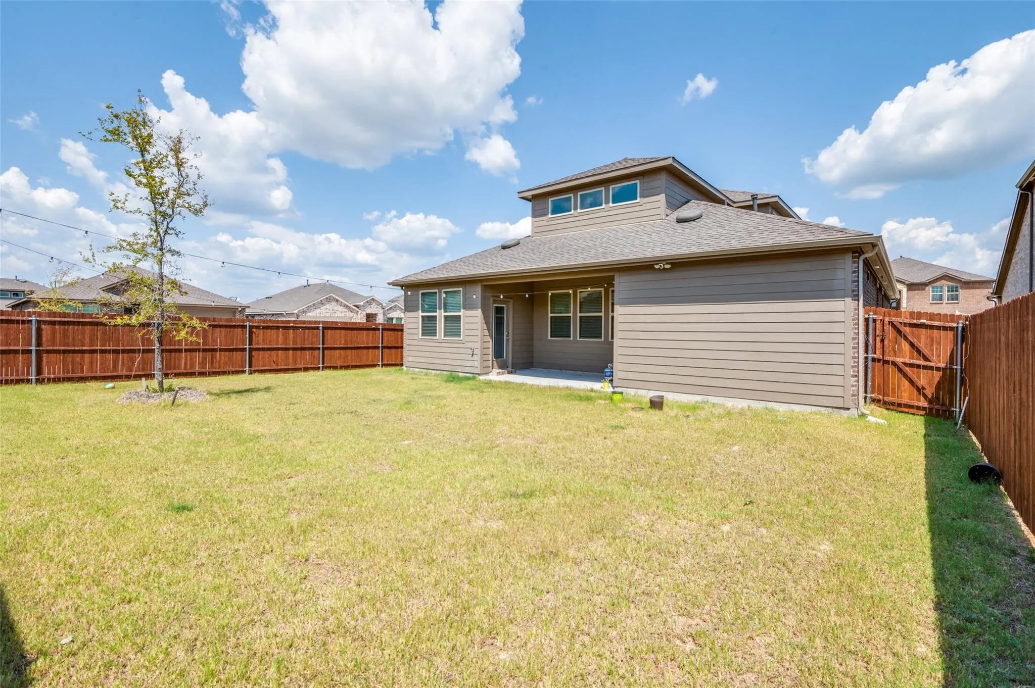 Expansive backyard featuring a privacy fence, a concrete patio, and a dormer with multiple windows