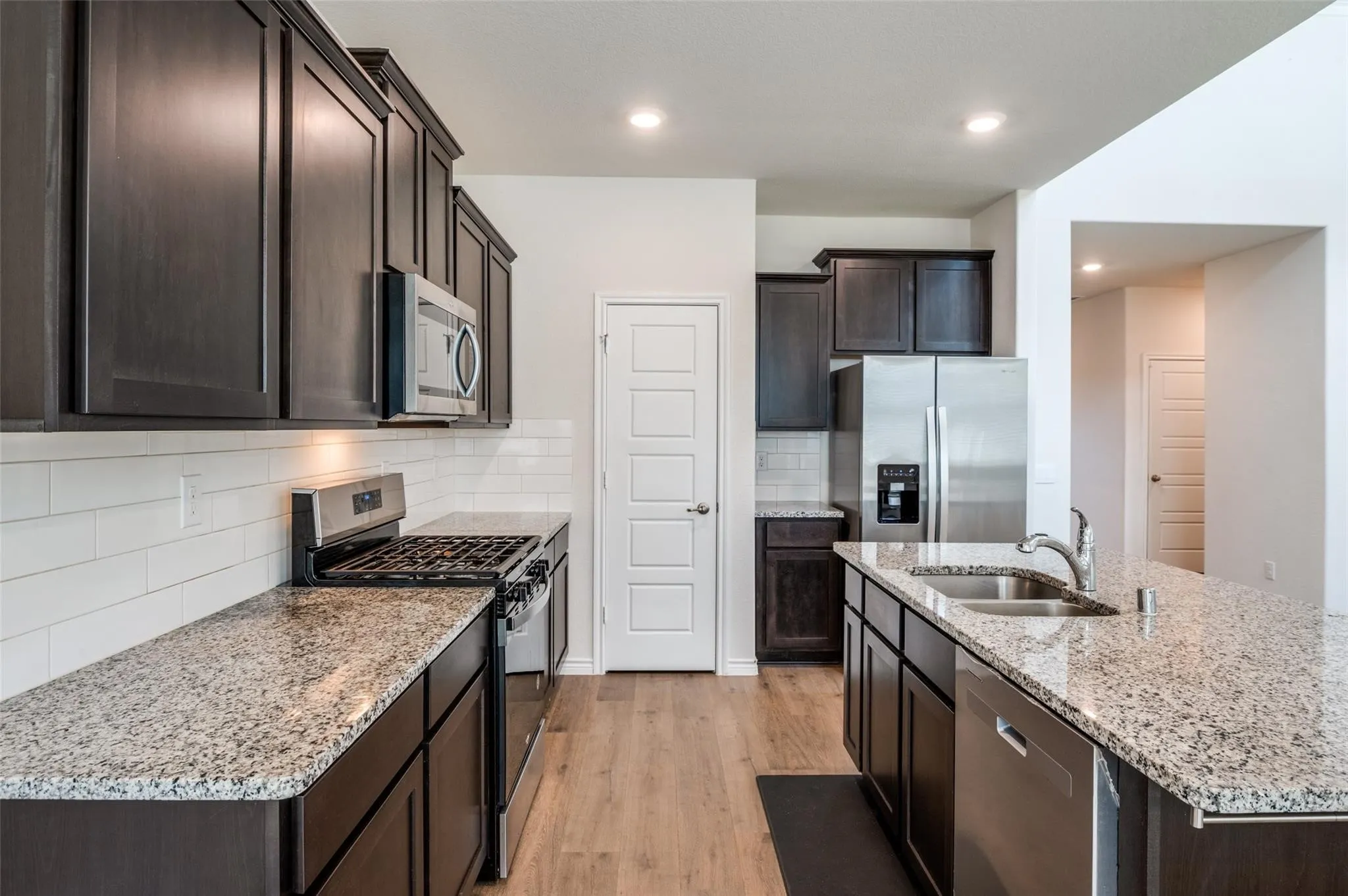 Kitchen featuring dark wood-finish cabinetry, stainless steel appliances, granite countertops, wood-finish flooring, and a subway tile backsplash