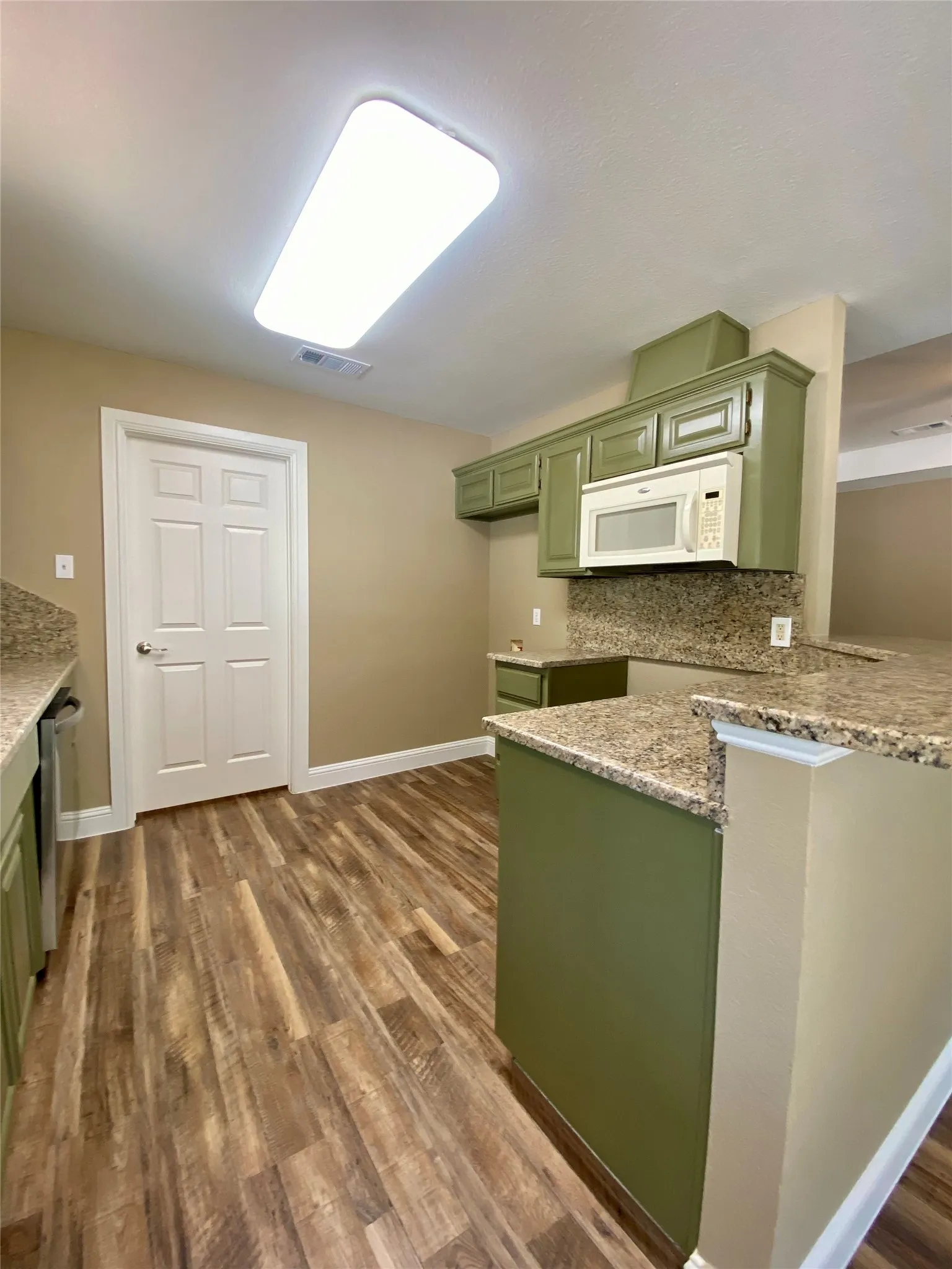 Kitchen featuring wood-finish flooring, green cabinetry, granite countertops, and an integrated microwave