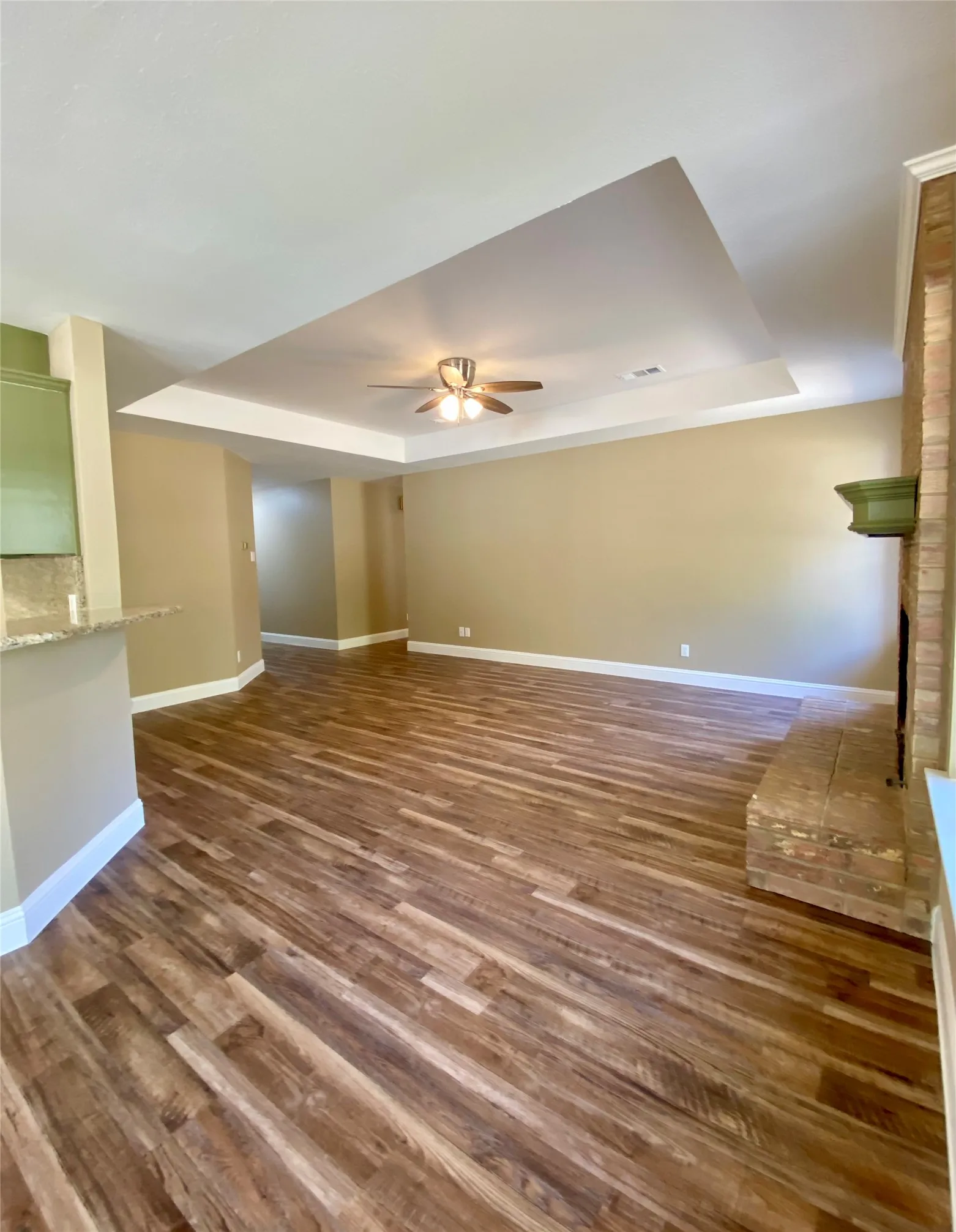 Tray ceiling with a ceiling fan, wood-finish flooring, and a brick fireplace