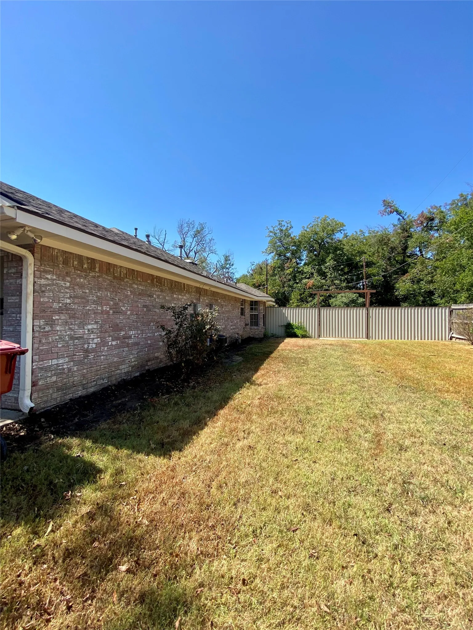 North elevation brick exterior, sloped shingle roof, established landscaping, privacy fencing, and a spacious side yard