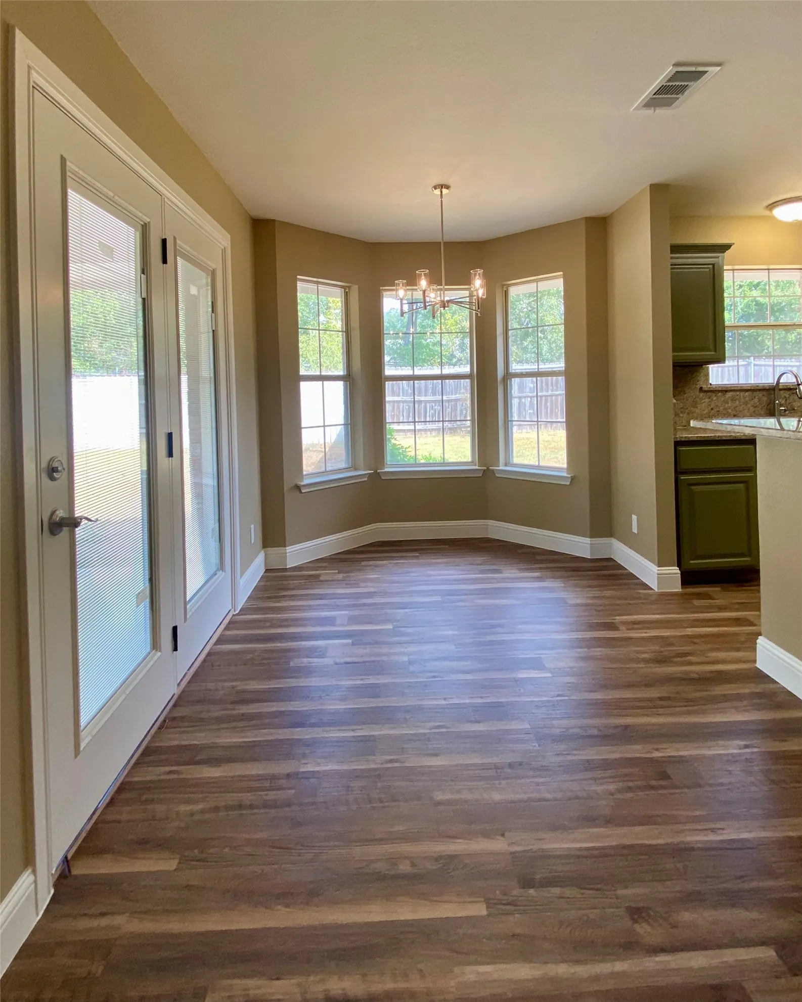 Wood-finish flooring throughout, bay window with multiple panes, modern chandelier, and double French doors with frosted panels