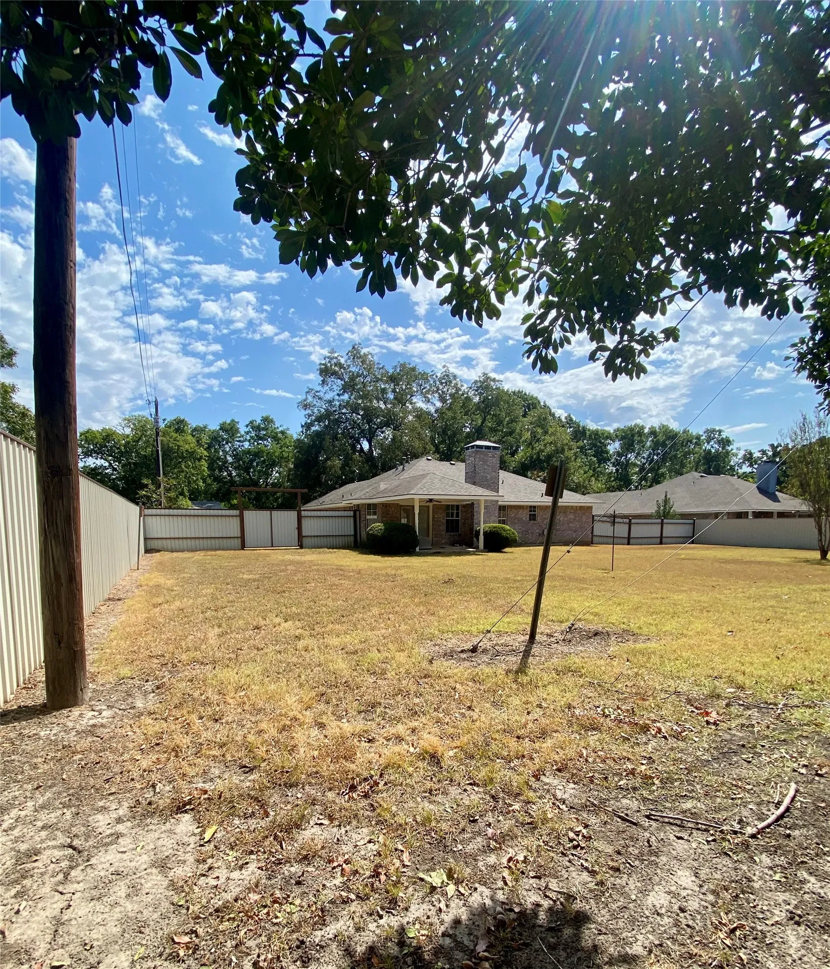 NW corner of Expansive rear yard featuring a partial corrugated metal fence, partial wood fence, and mature trees