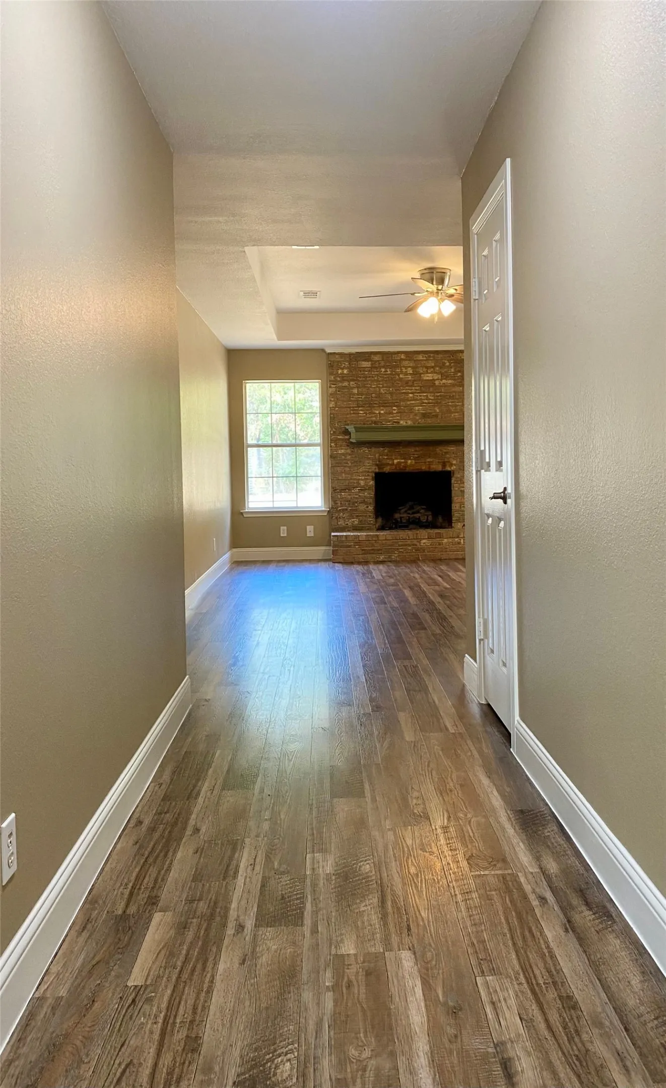 Wood-finish flooring throughout, tray ceiling, and a brick fireplace