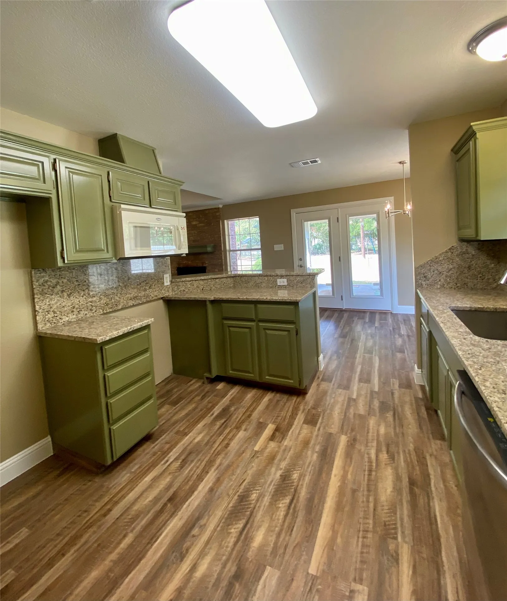 Kitchen featuring wood-finish flooring, green cabinetry, granite countertops, and a built-in microwave