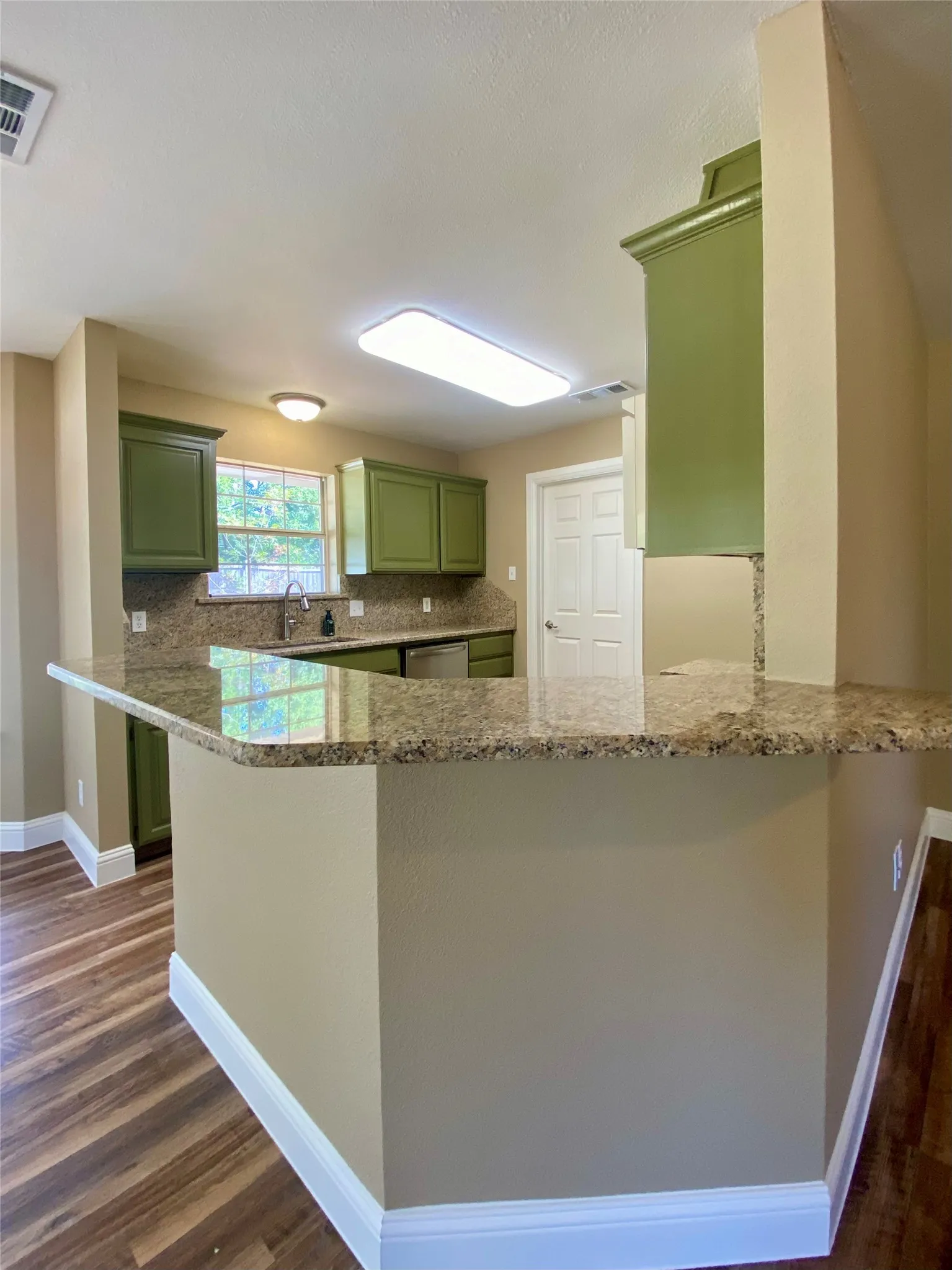 Kitchen with granite countertops, wood-finish flooring, green cabinetry, and stainless steel dishwasher