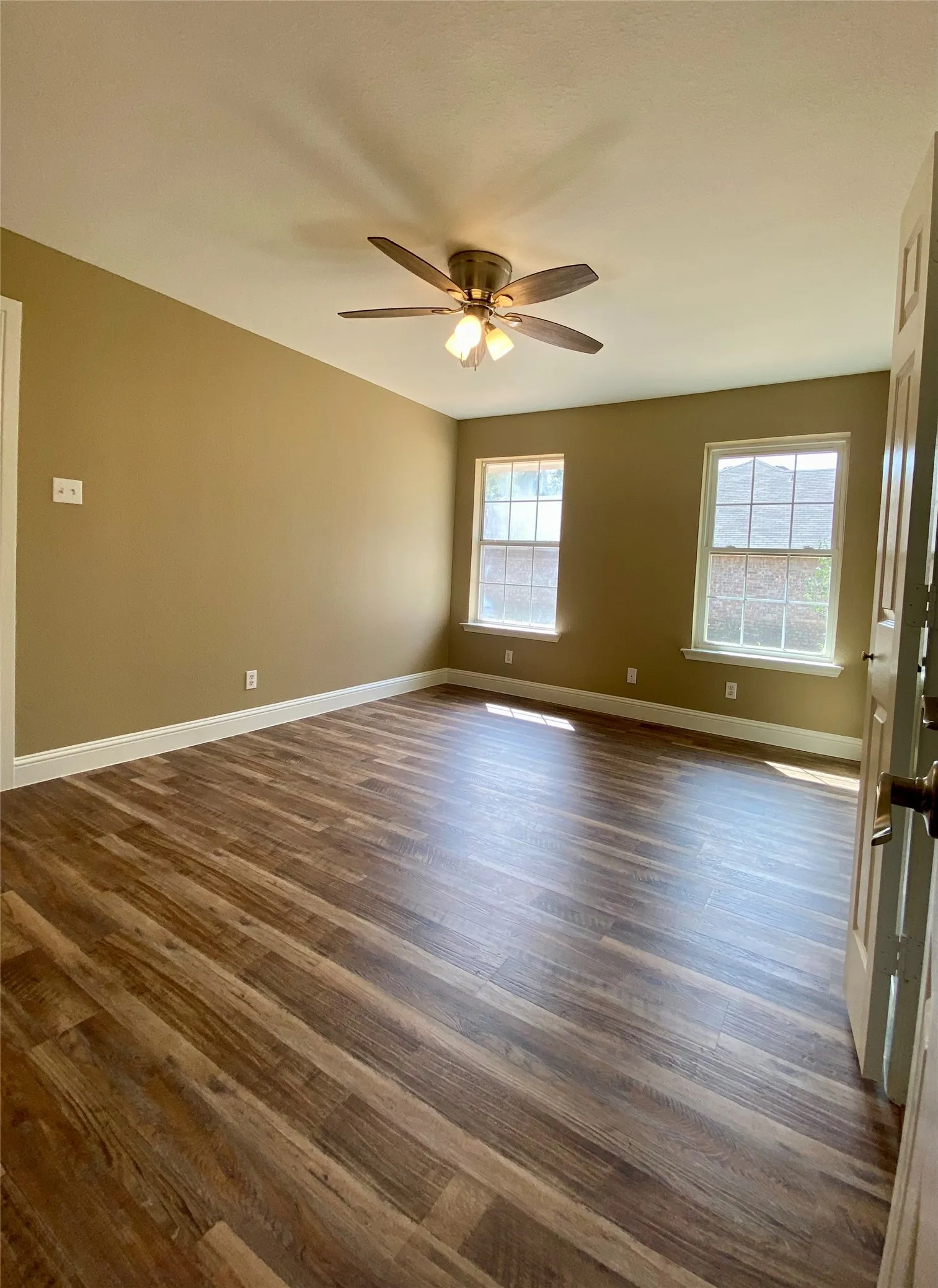 Wood-finish flooring, ceiling fan with integrated lighting, multiple windows, and painted walls
