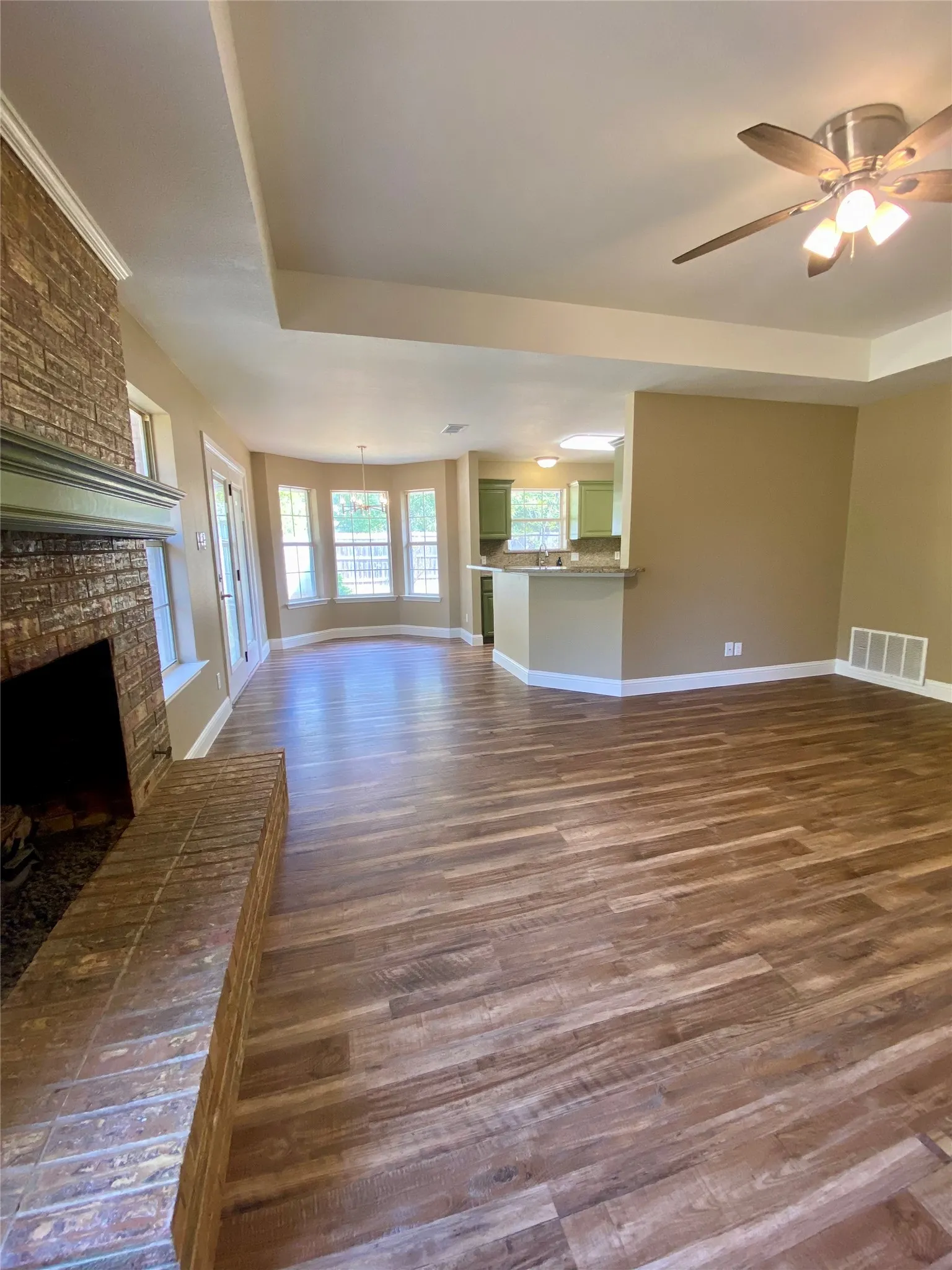 Expansive living area featuring wood-finish flooring, a brick fireplace with a mantel, and a ceiling fan with integrated lighting