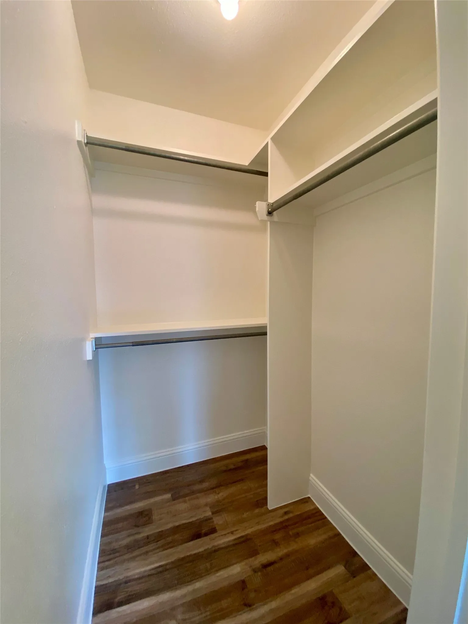 Primary Walk-in closet #2 featuring wood-finish flooring, white walls, built-in shelving, and metal hanging rods